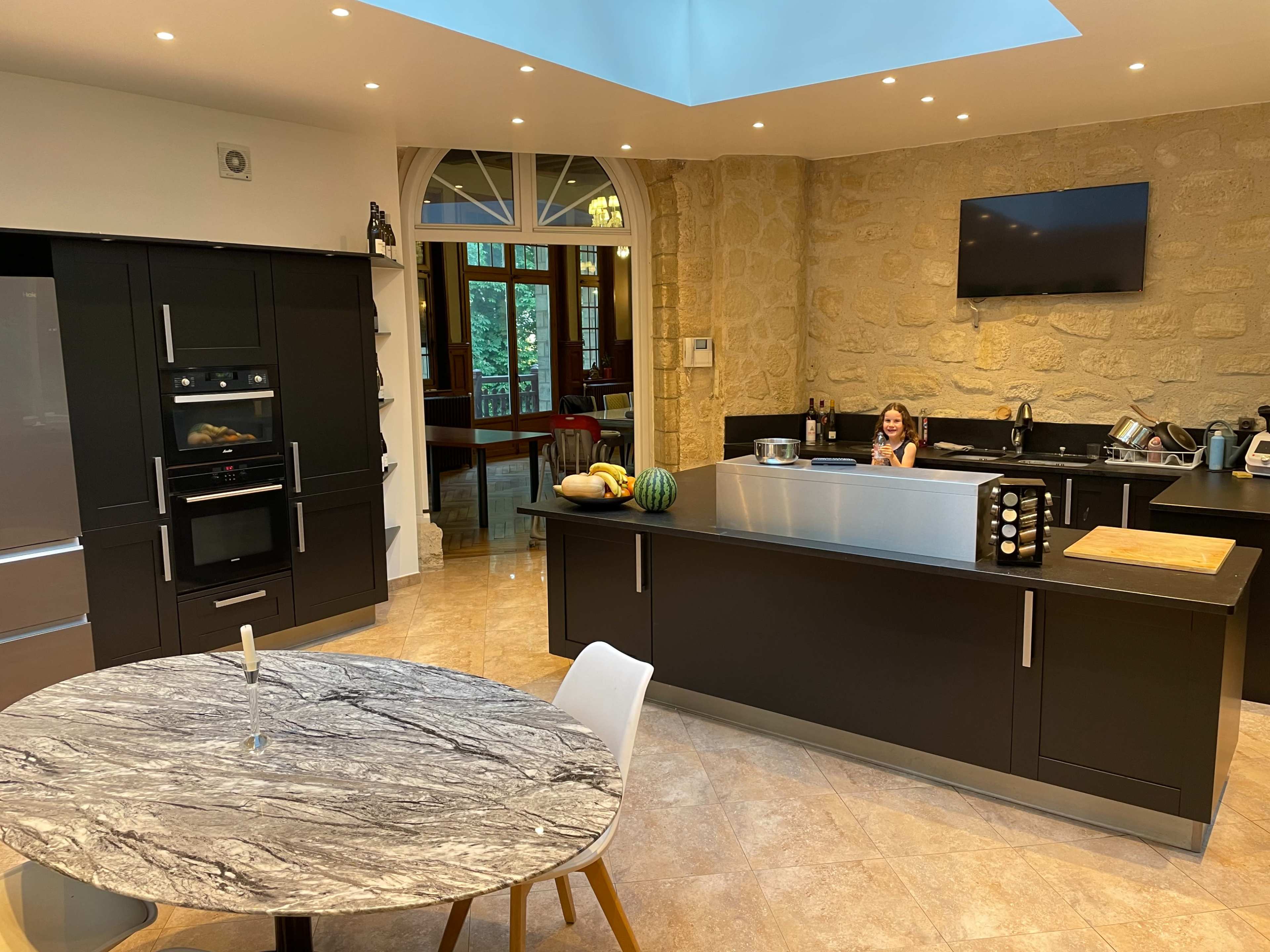 A modern kitchen features a large island with a stone countertop, built-in appliances, and a view of a window overlooking a dining area.