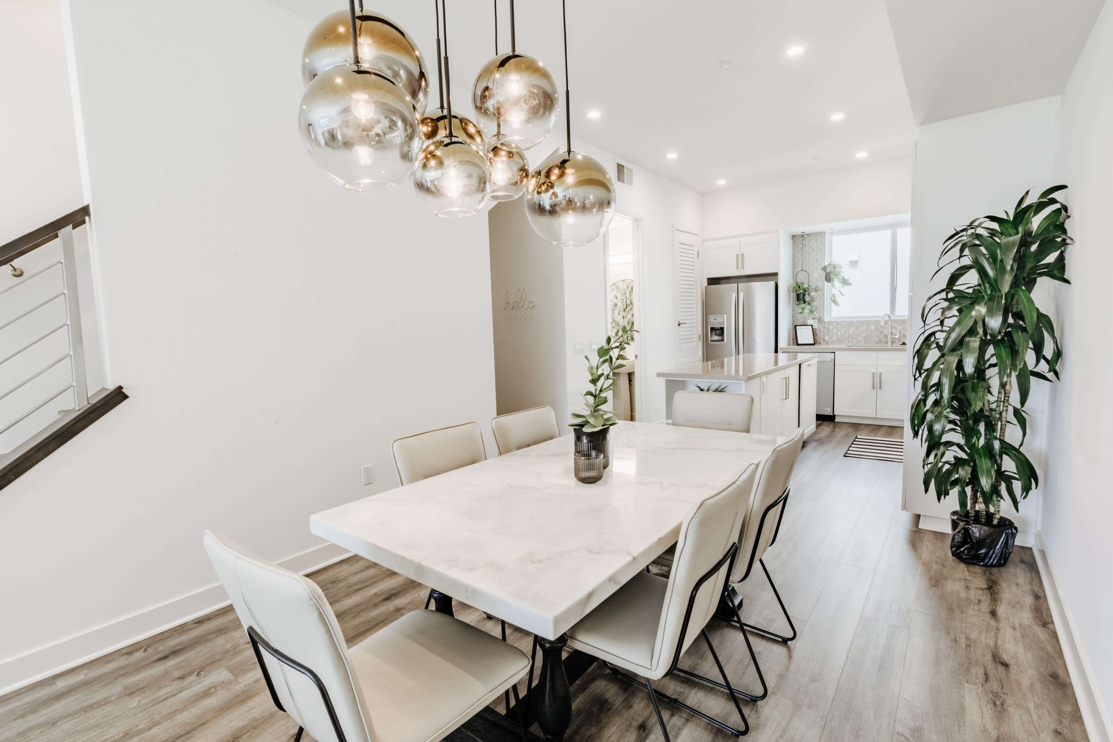 A modern dining area features a marble table surrounded by beige chairs, with a cluster of globe-shaped pendant lights hanging above.