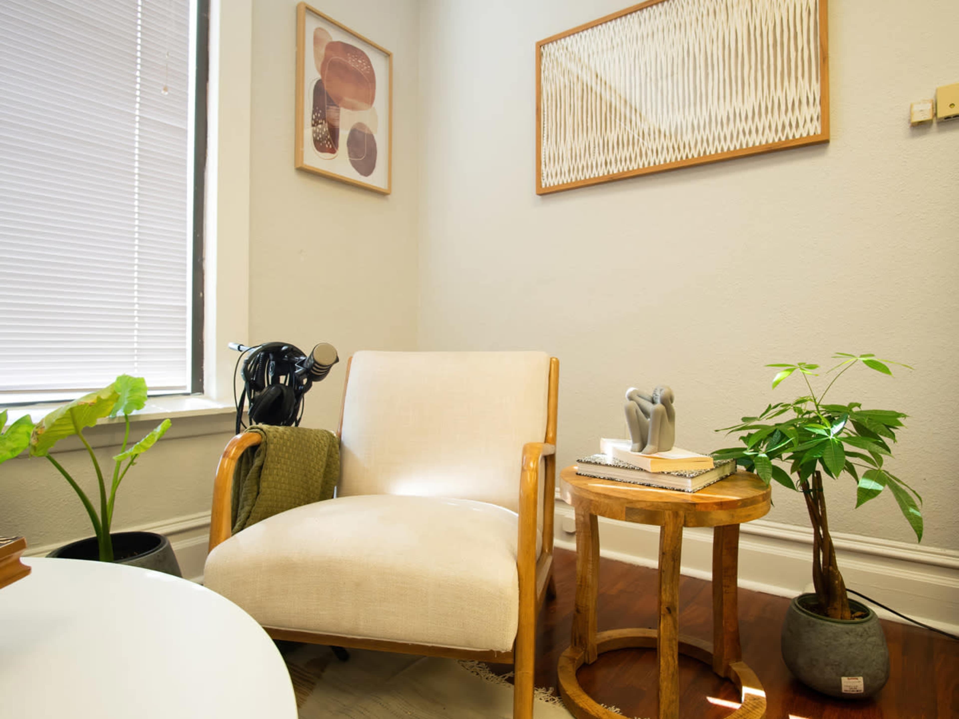 A cozy corner of a room featuring a light-colored armchair, a wooden side table, a plant, and framed artwork on the walls.