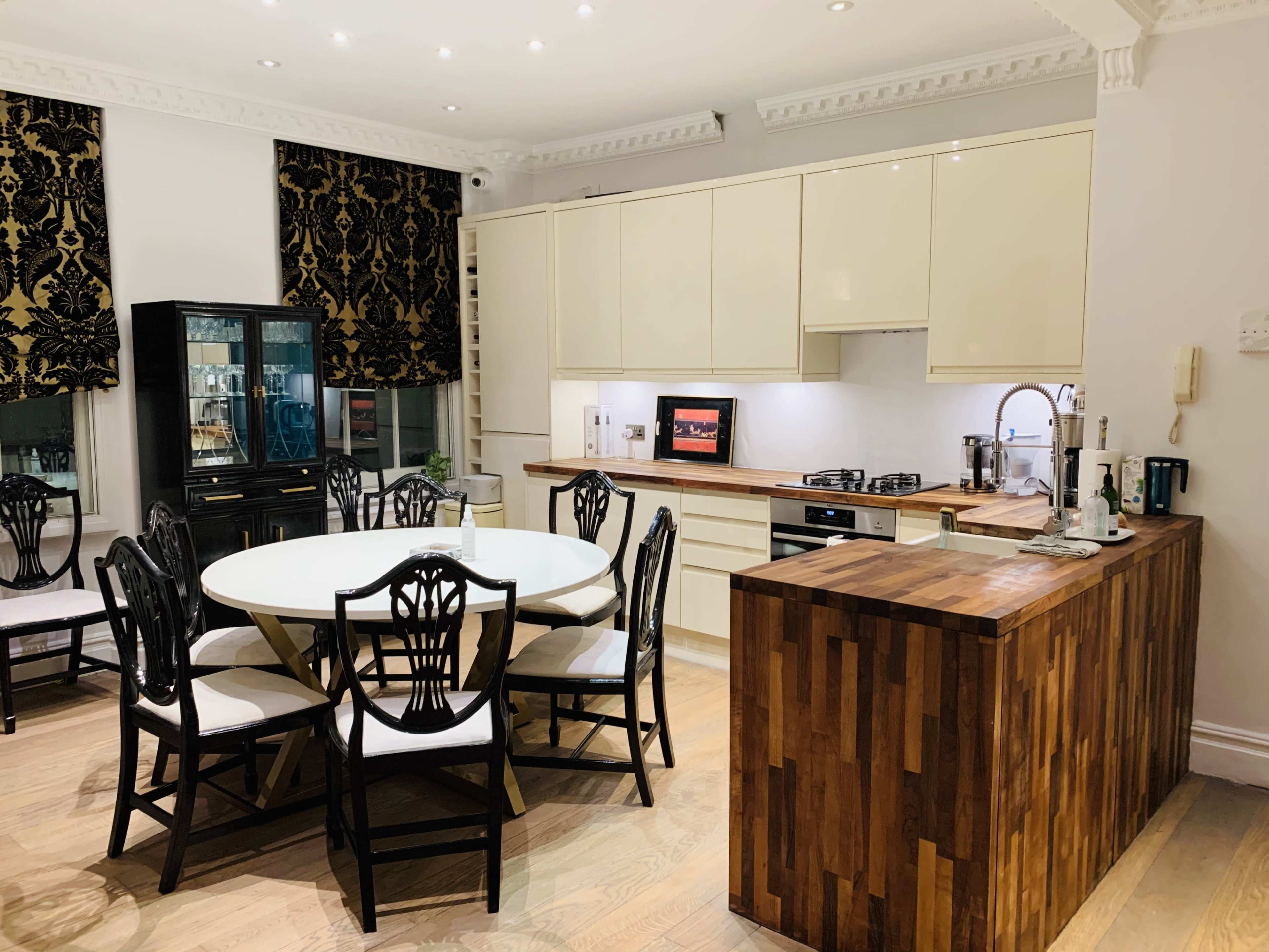 A modern kitchen features a round dining table surrounded by black wooden chairs, a wooden counter, and white cabinetry.