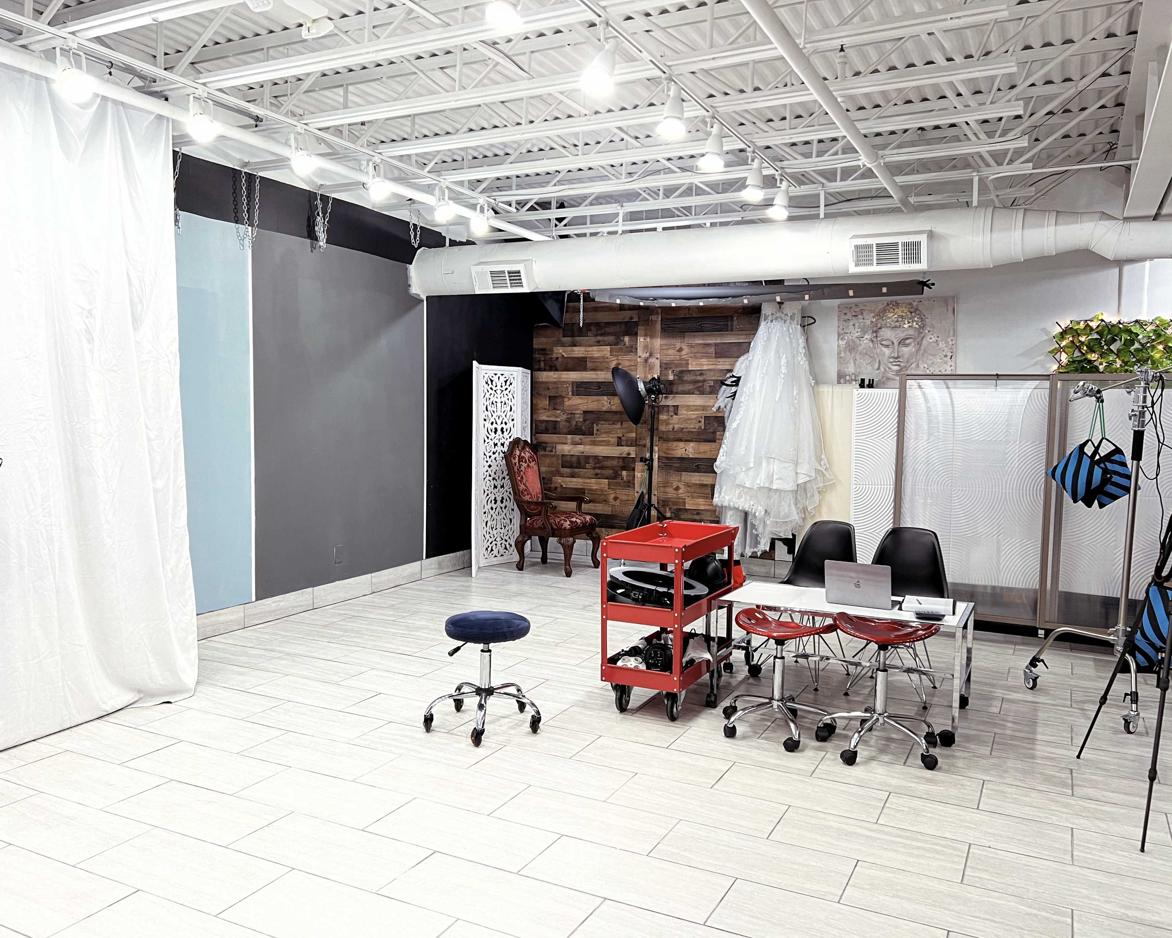 A spacious studio featuring a mix of decorative elements, including a wedding dress display, chairs, and various work stations.