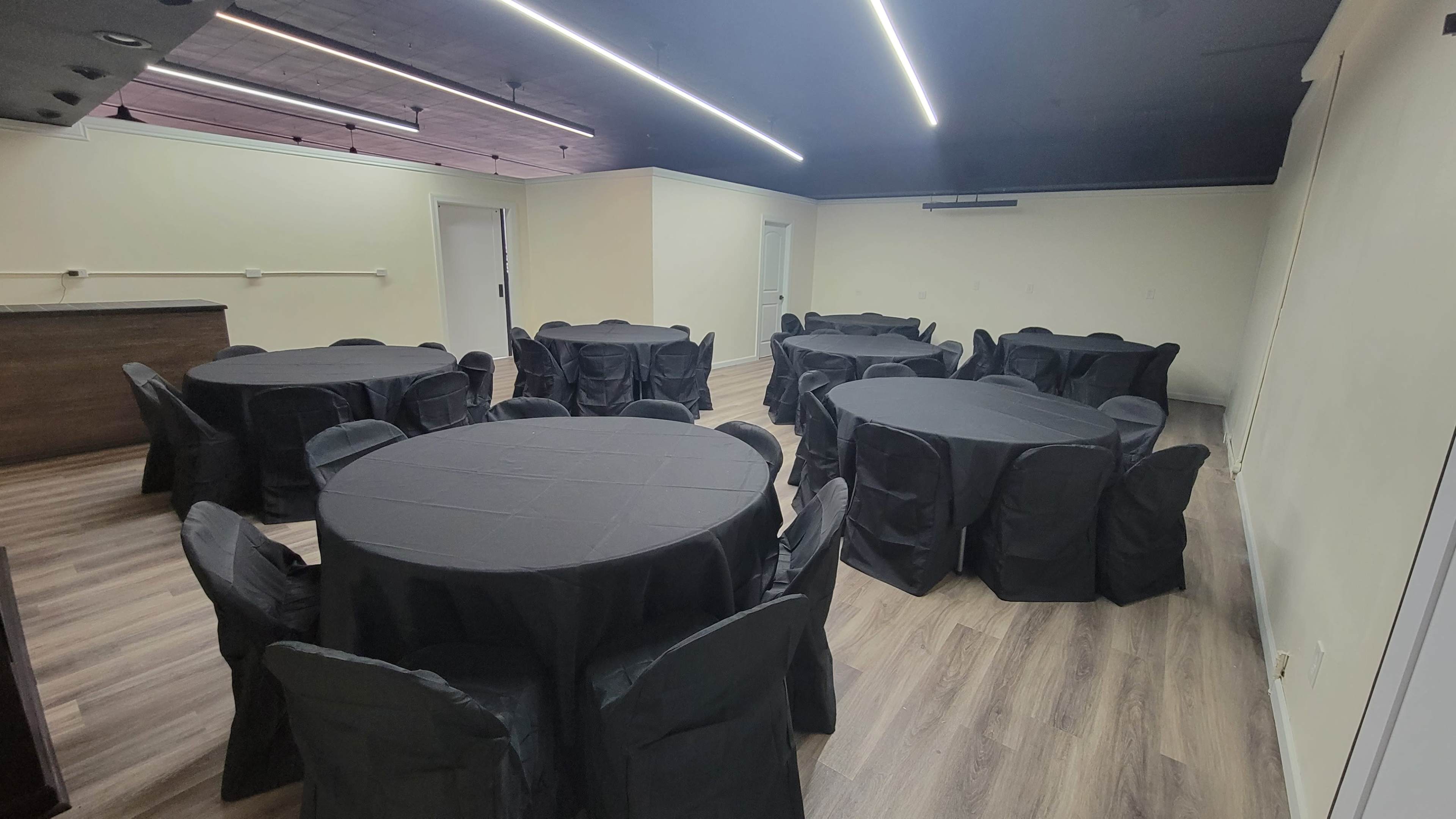 The image shows a spacious event room set with multiple round tables covered in black cloth and surrounded by matching chairs.