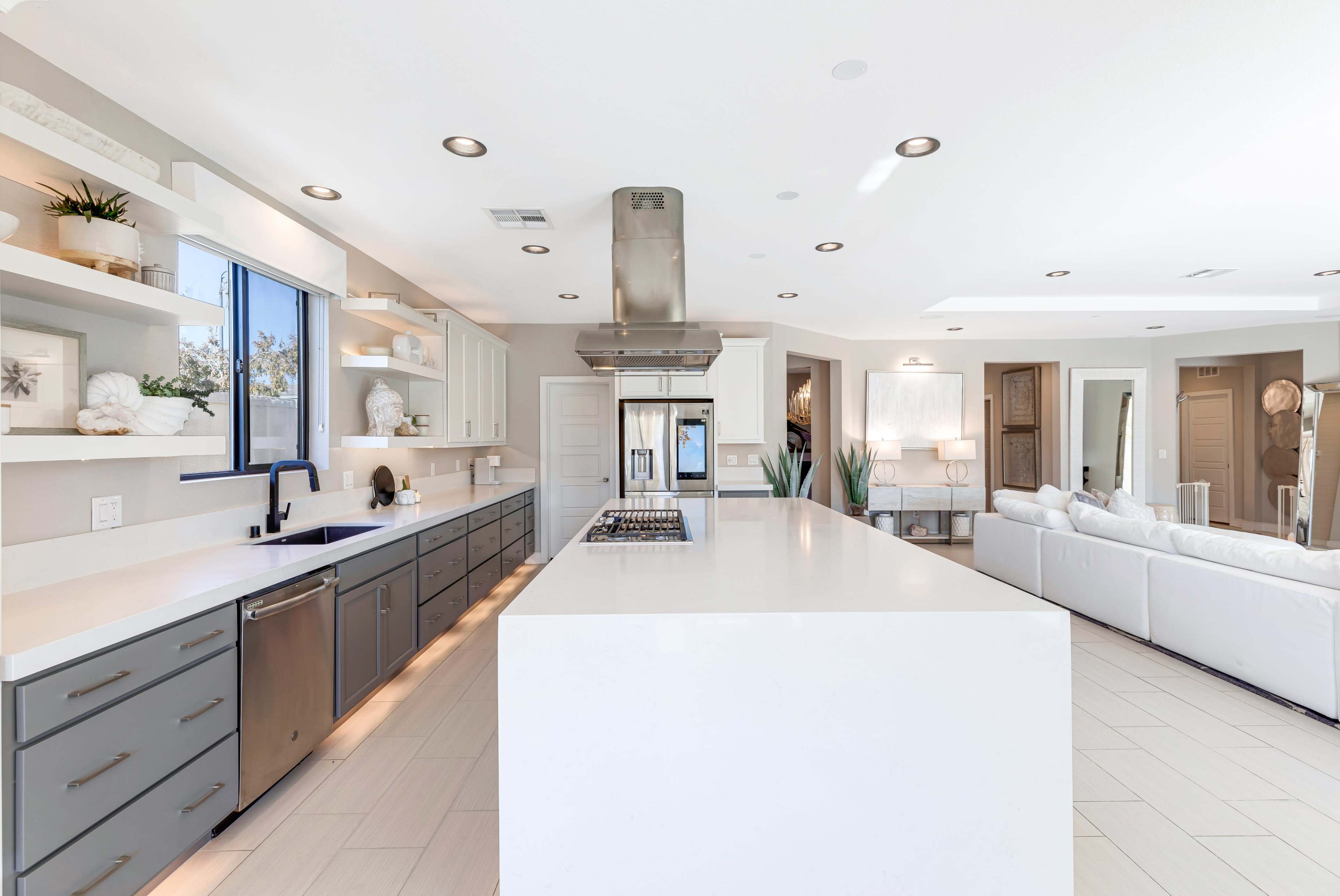 A modern kitchen with gray and white cabinetry, a large central island, and a stainless steel range hood.