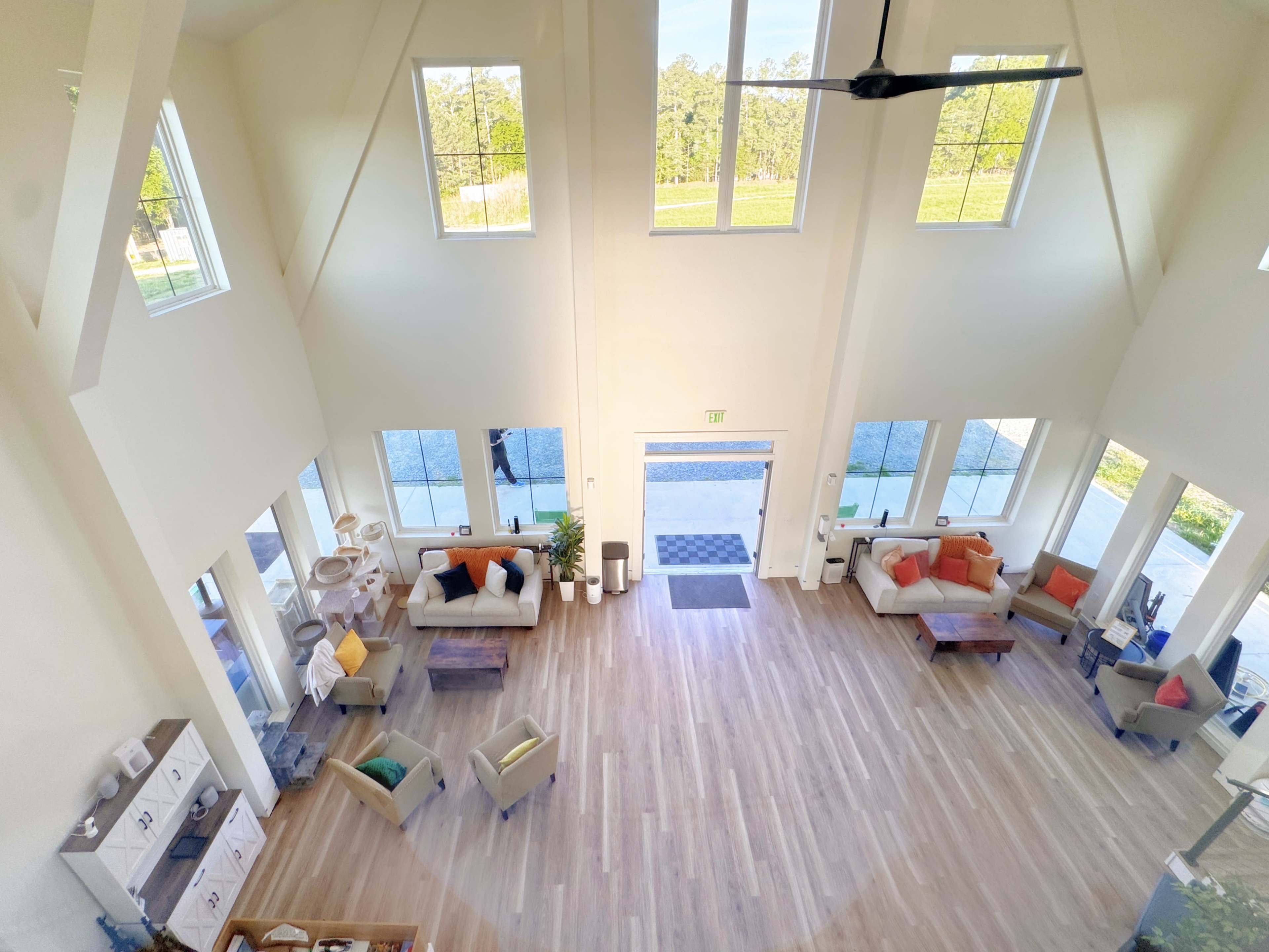 The image shows a spacious, well-lit living room with large windows, modern furniture, and a view of a landscaped outdoor area.