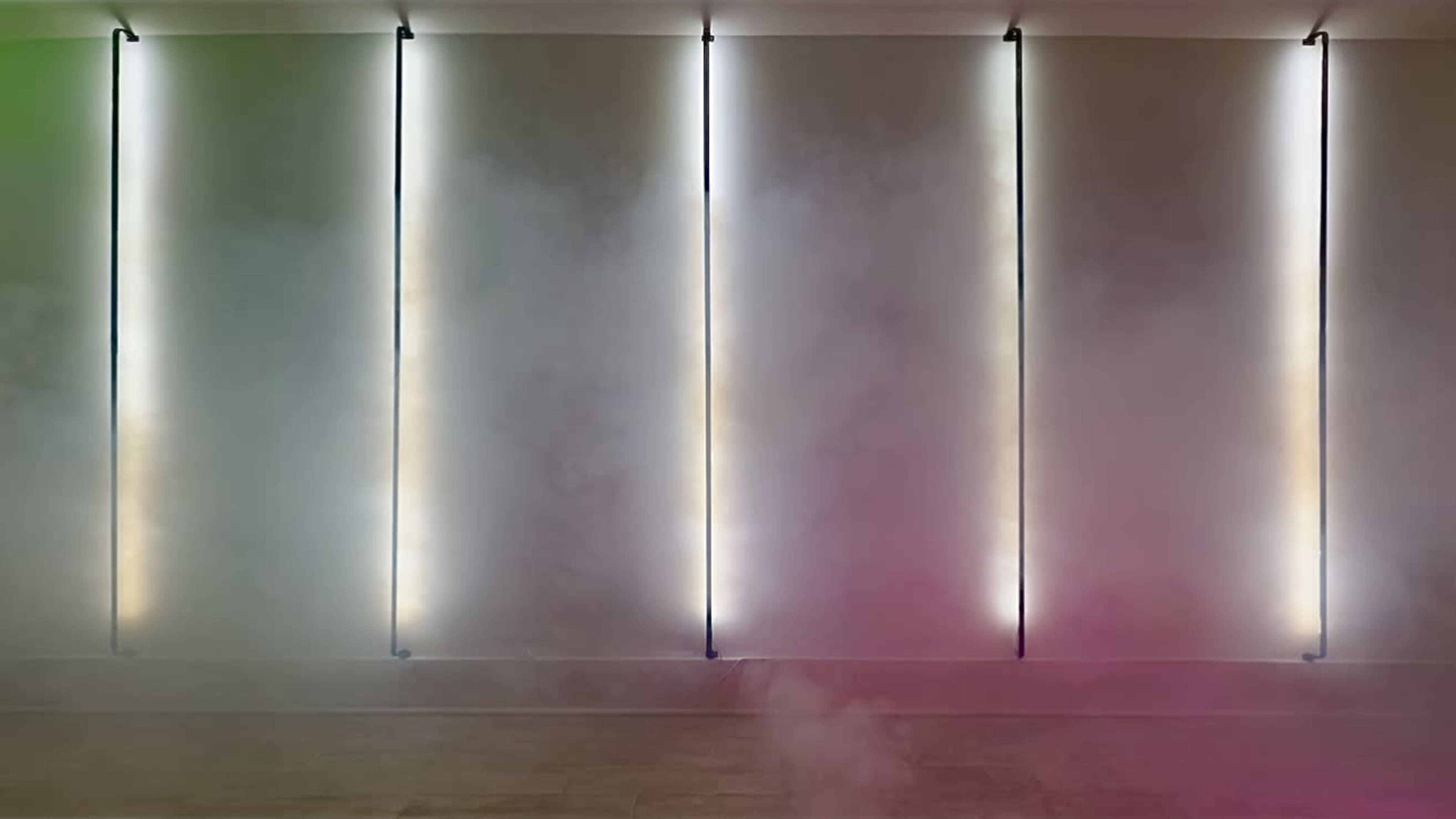 The image features a series of vertical light strips against a wall, surrounded by fog that creates a colorful ambiance.