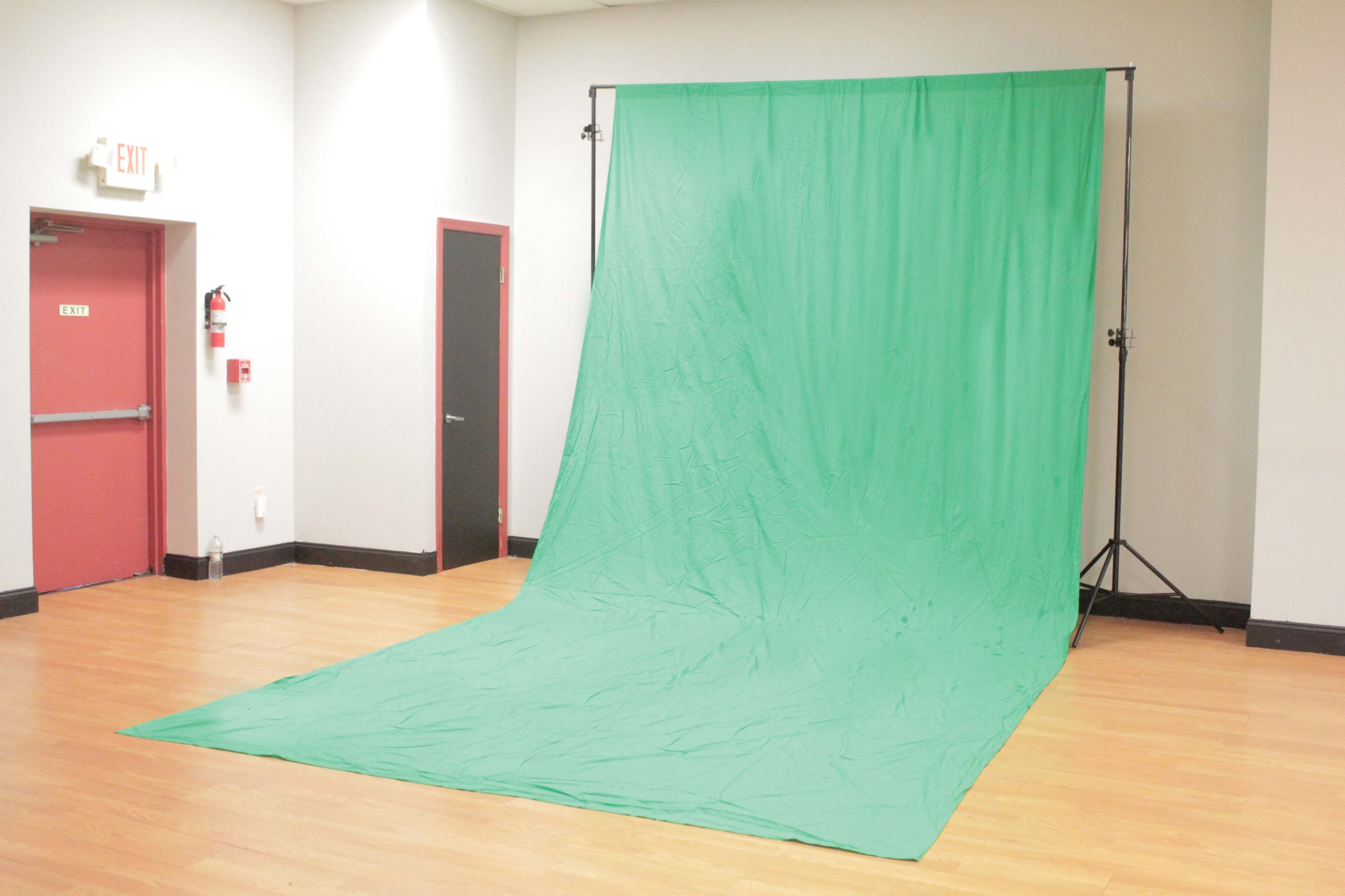 A green backdrop set up in a room with wooden flooring and plain walls.