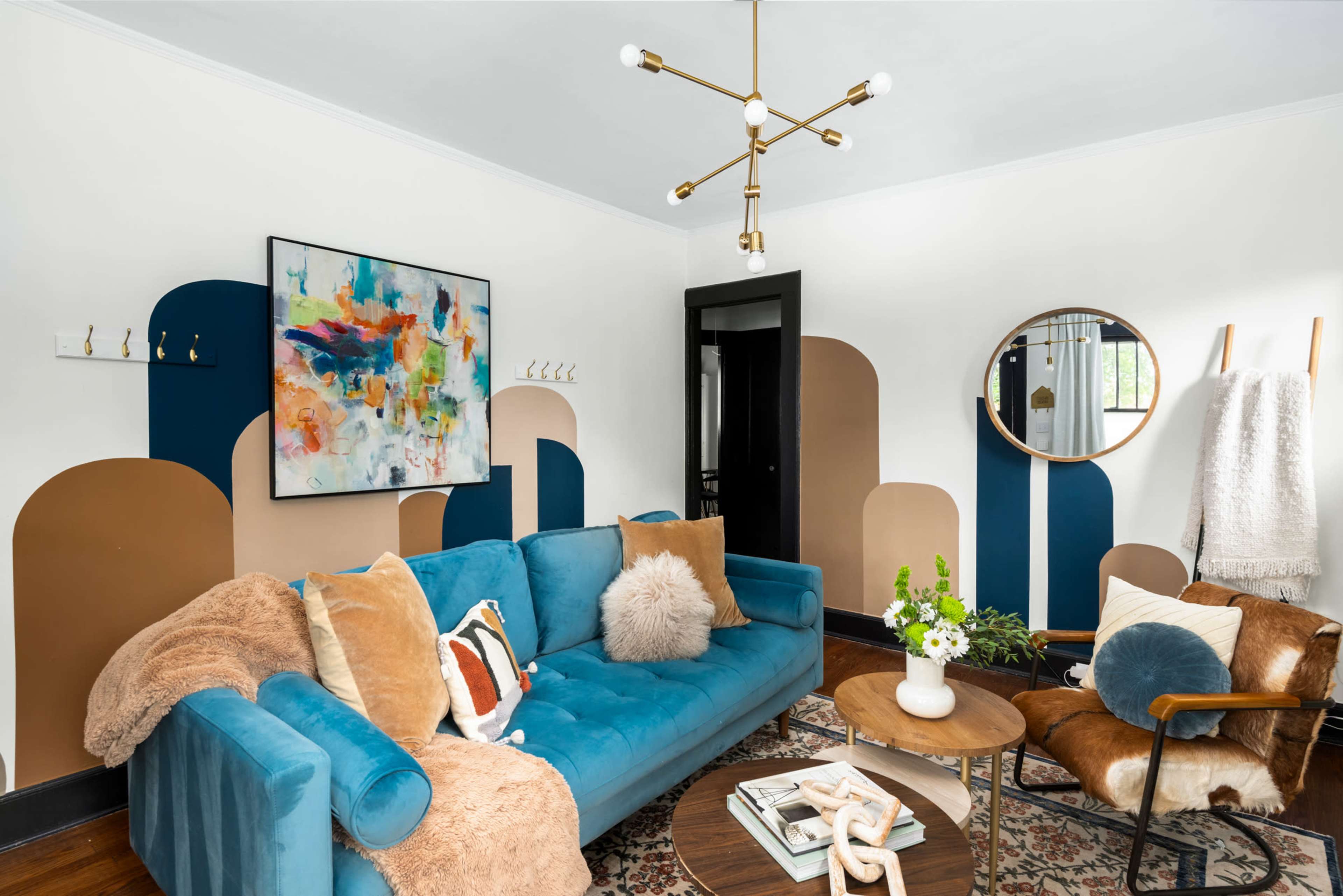 A modern living room features a blue sofa, abstract wall art, and a round mirror, complemented by a wooden coffee table and decorative accents.