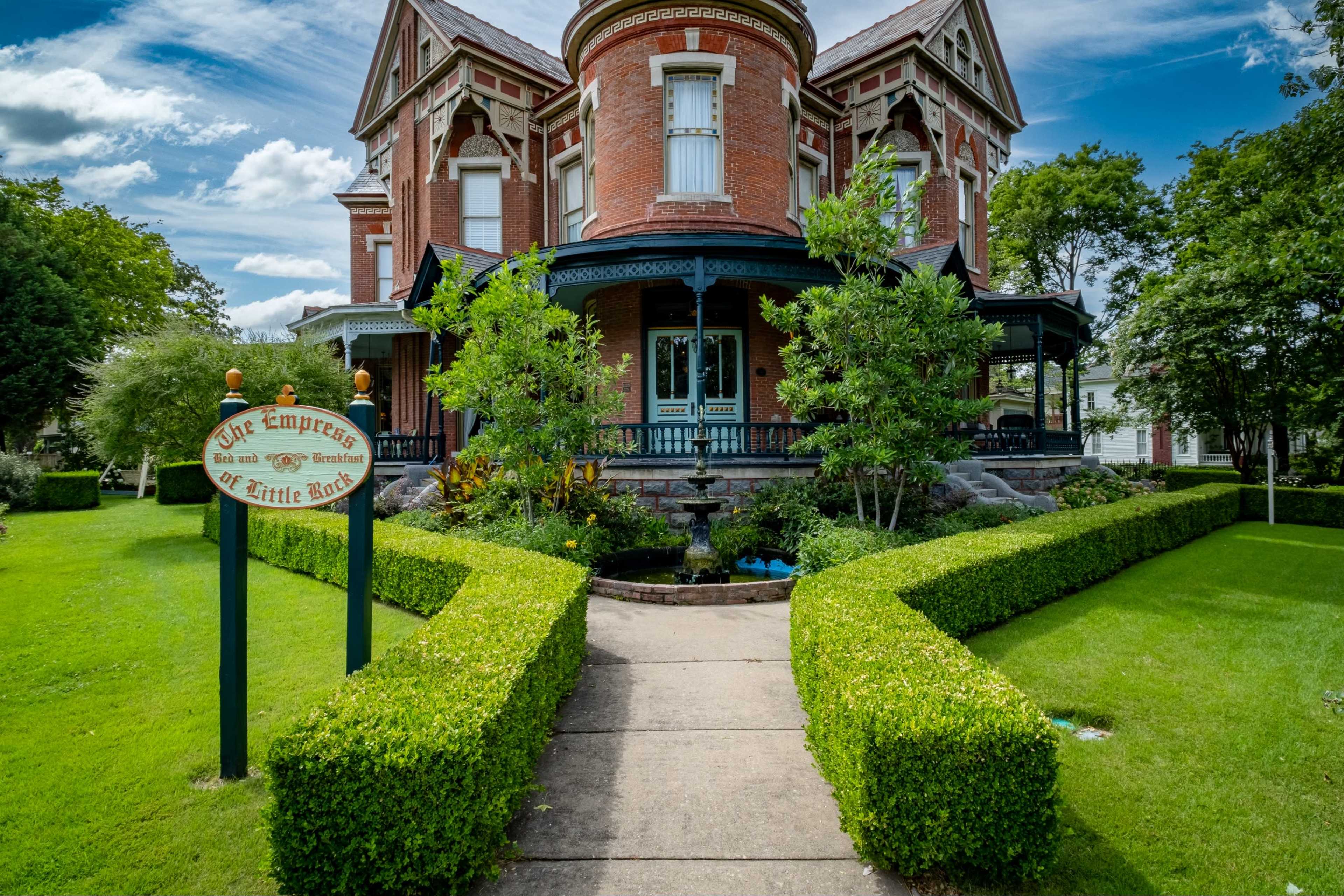 The image shows a Victorian-style brick house with a prominent porch, landscaped gardens, and a sign that reads "The Empress of Little Rock."