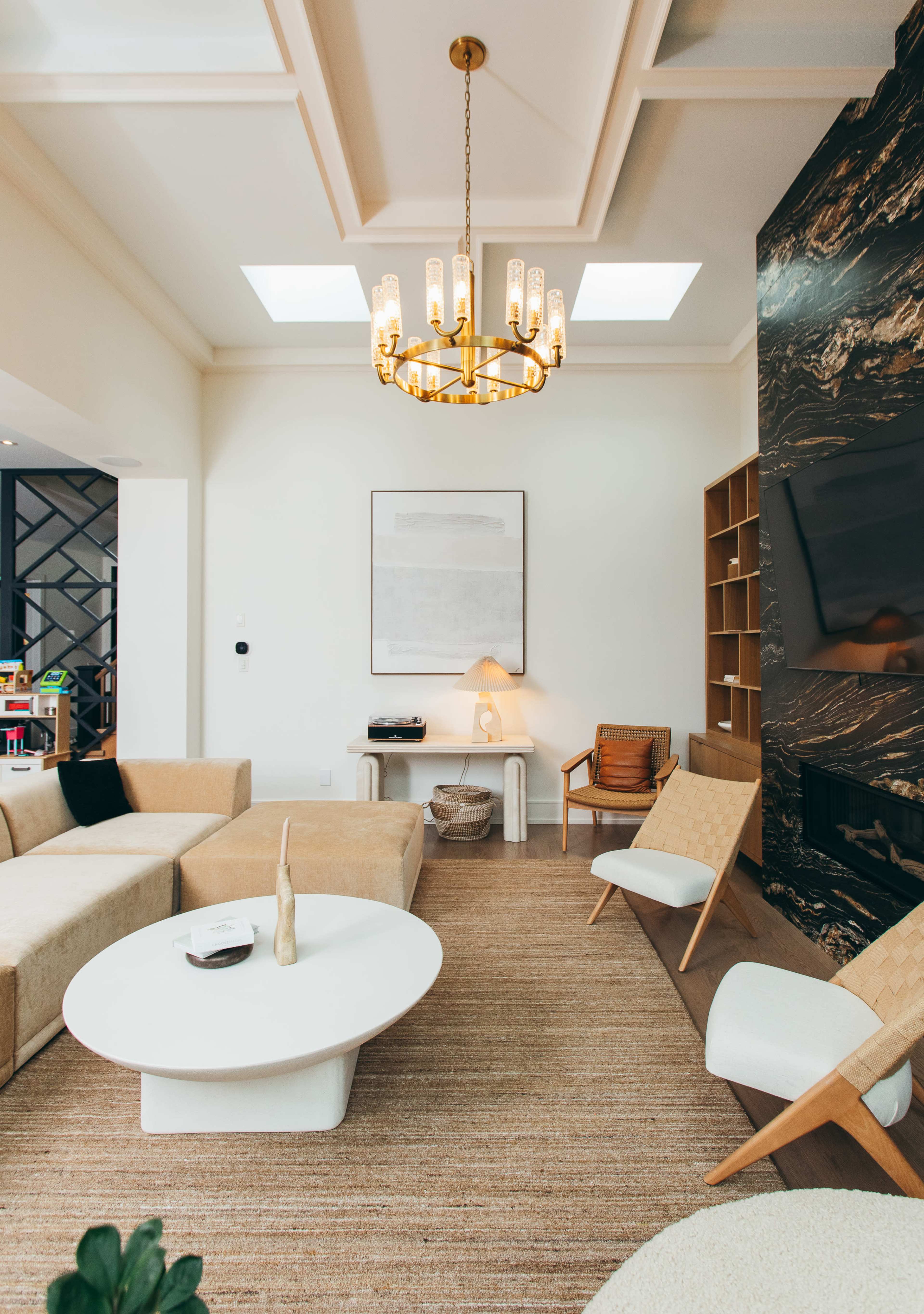 A modern living room features a large sectional sofa, a round white coffee table, a wooden chair, and a black stone accent wall with a television.