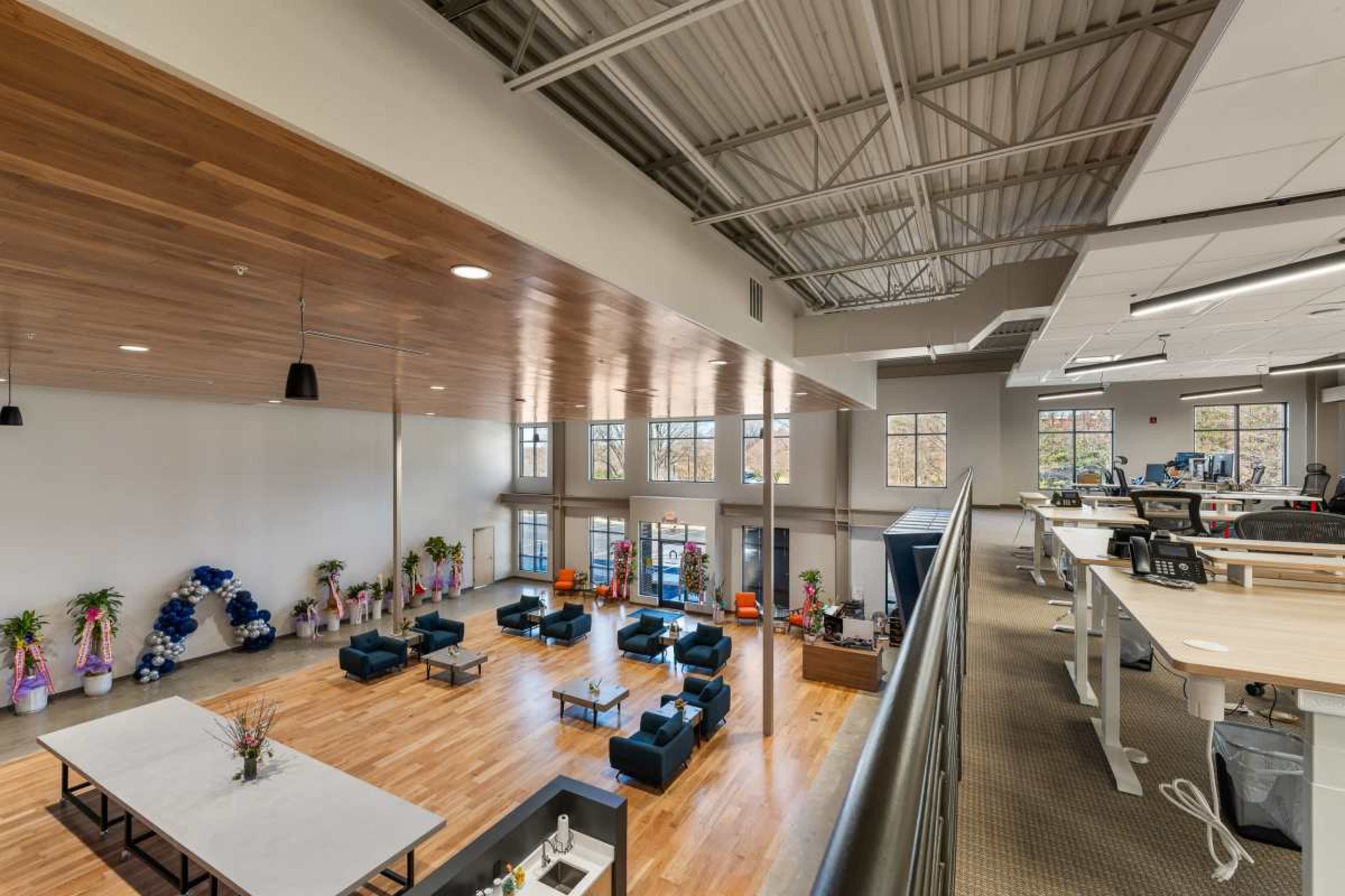 The image shows a spacious, modern office interior with seating areas, large windows, and an open layout.