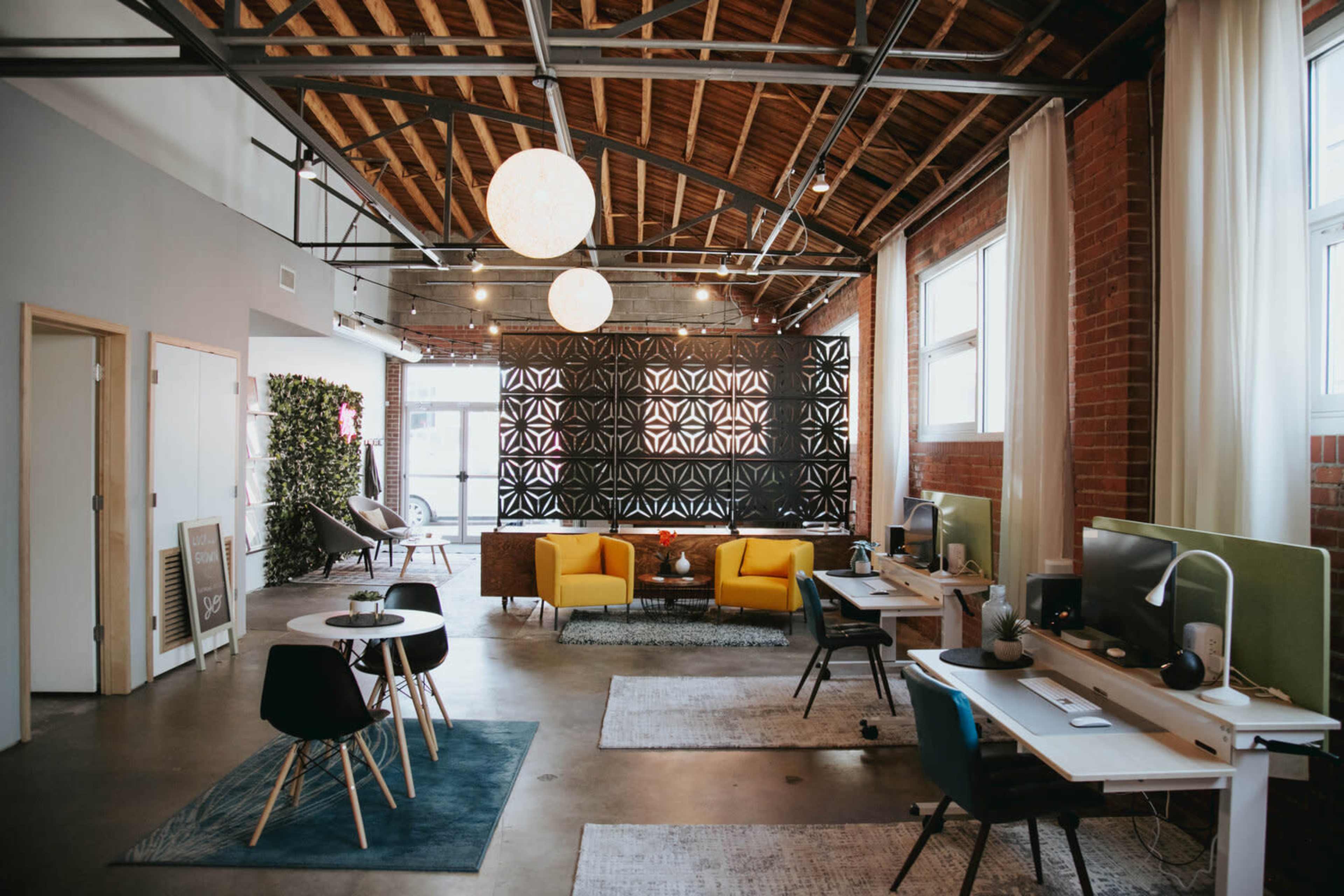 A modern open office space featuring yellow armchairs, a wall with decorative black panels, and multiple workstations with computers.