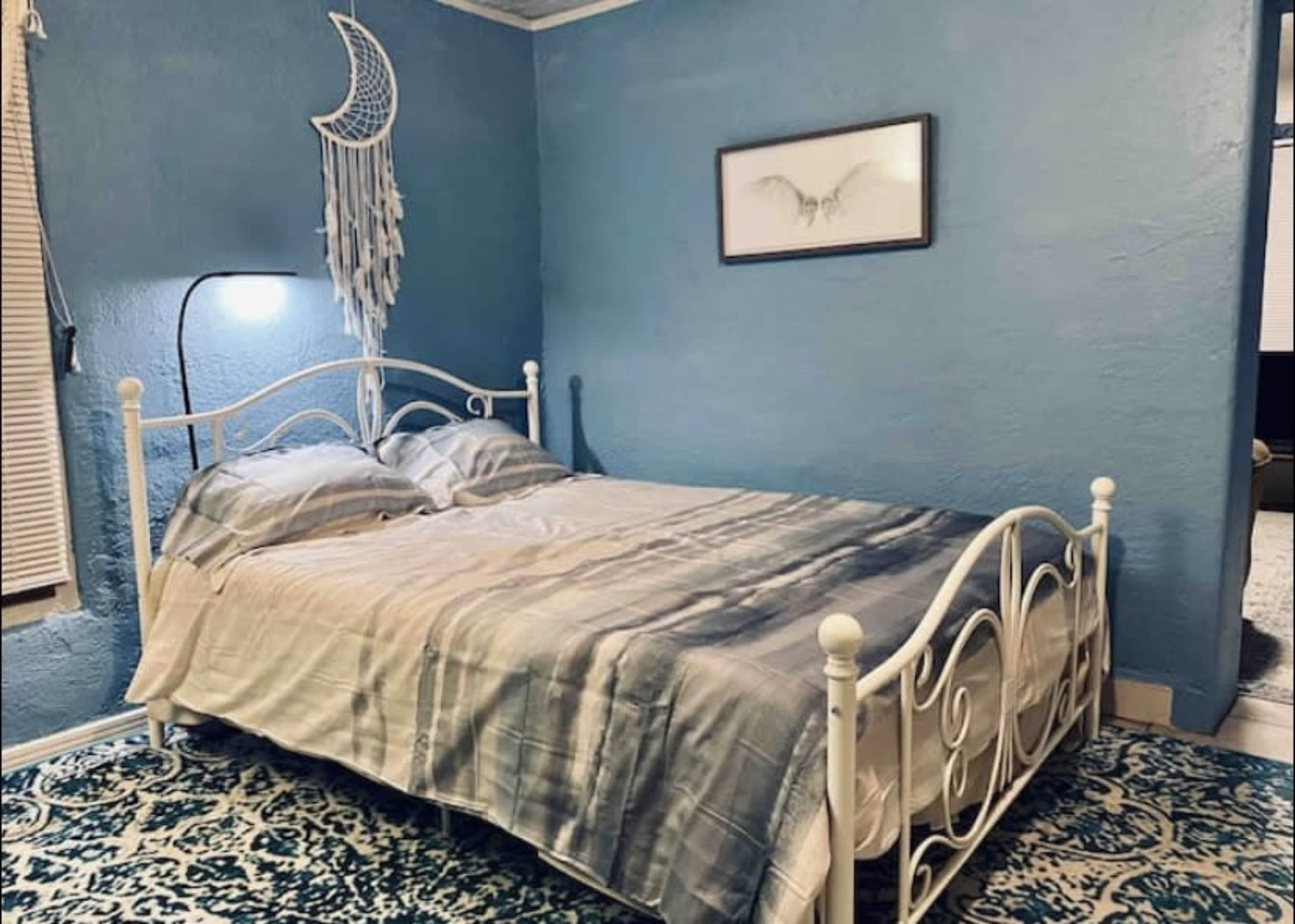 A bedroom with a white metal bed frame, blue walls, and a patterned rug.