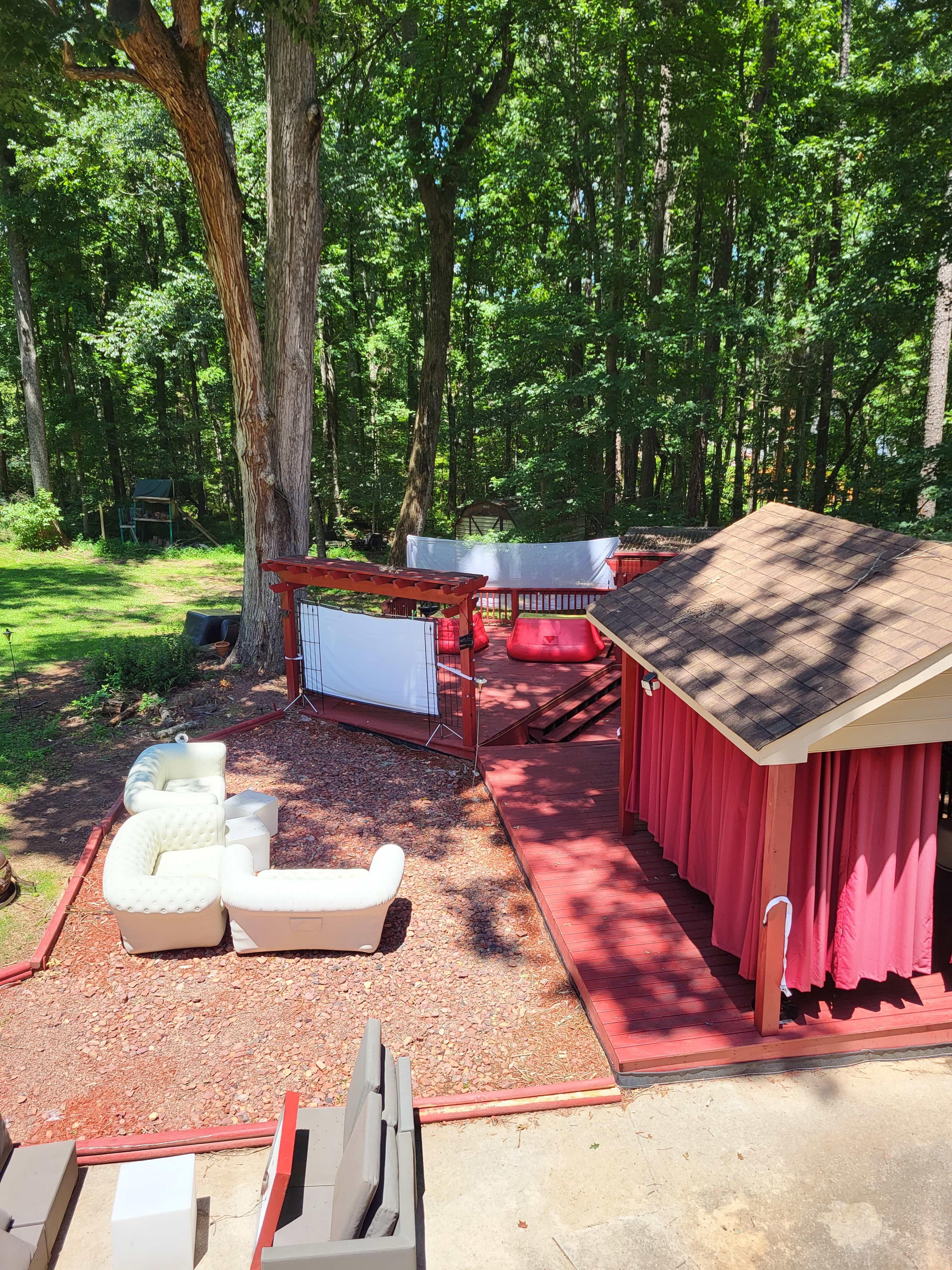 The image shows a backyard patio area with outdoor furniture, a gazebo, and a shed, surrounded by trees.