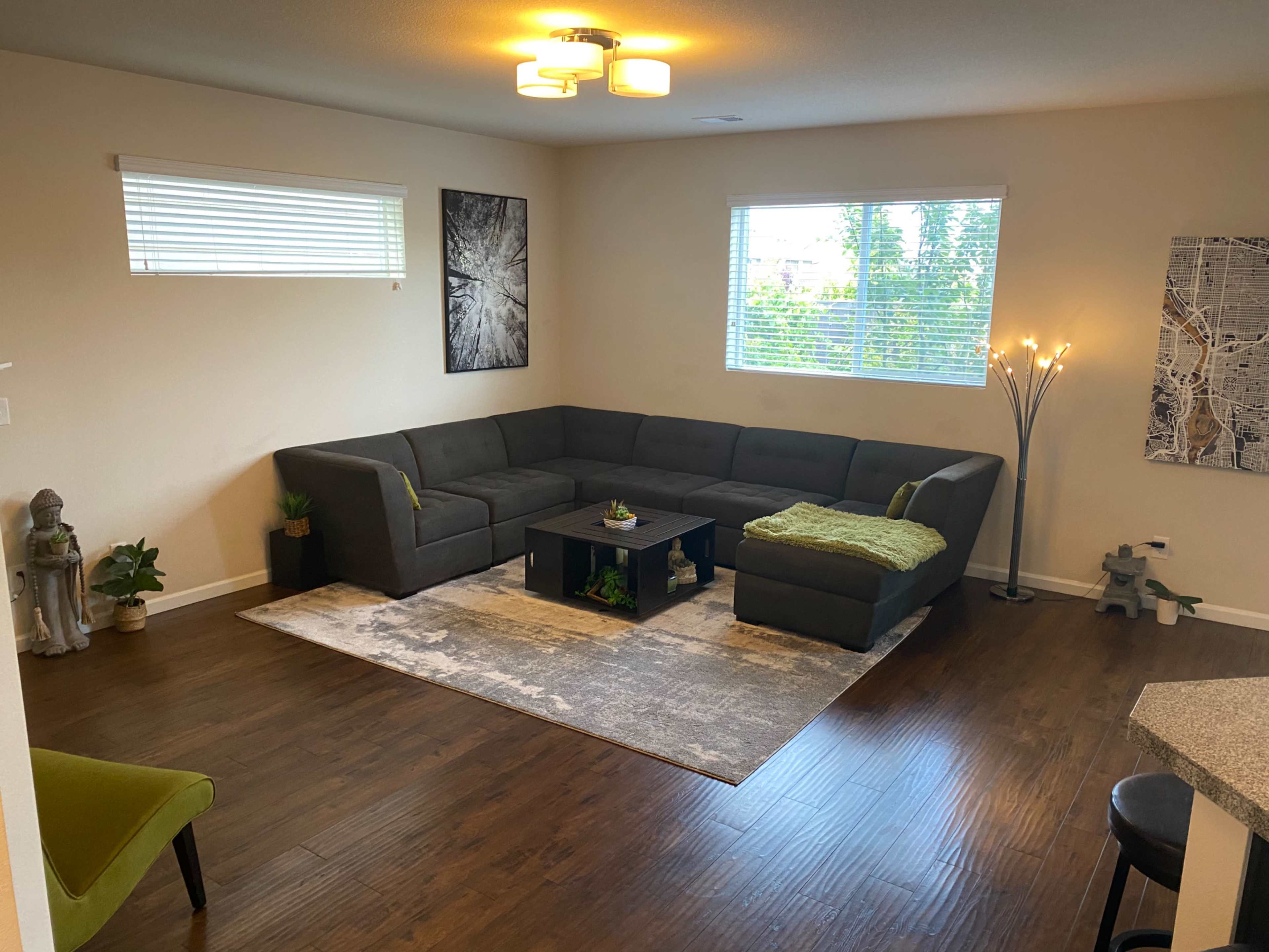 A modern living room with a sectional sofa, a coffee table, a decorative rug, and large windows allowing natural light to enter.