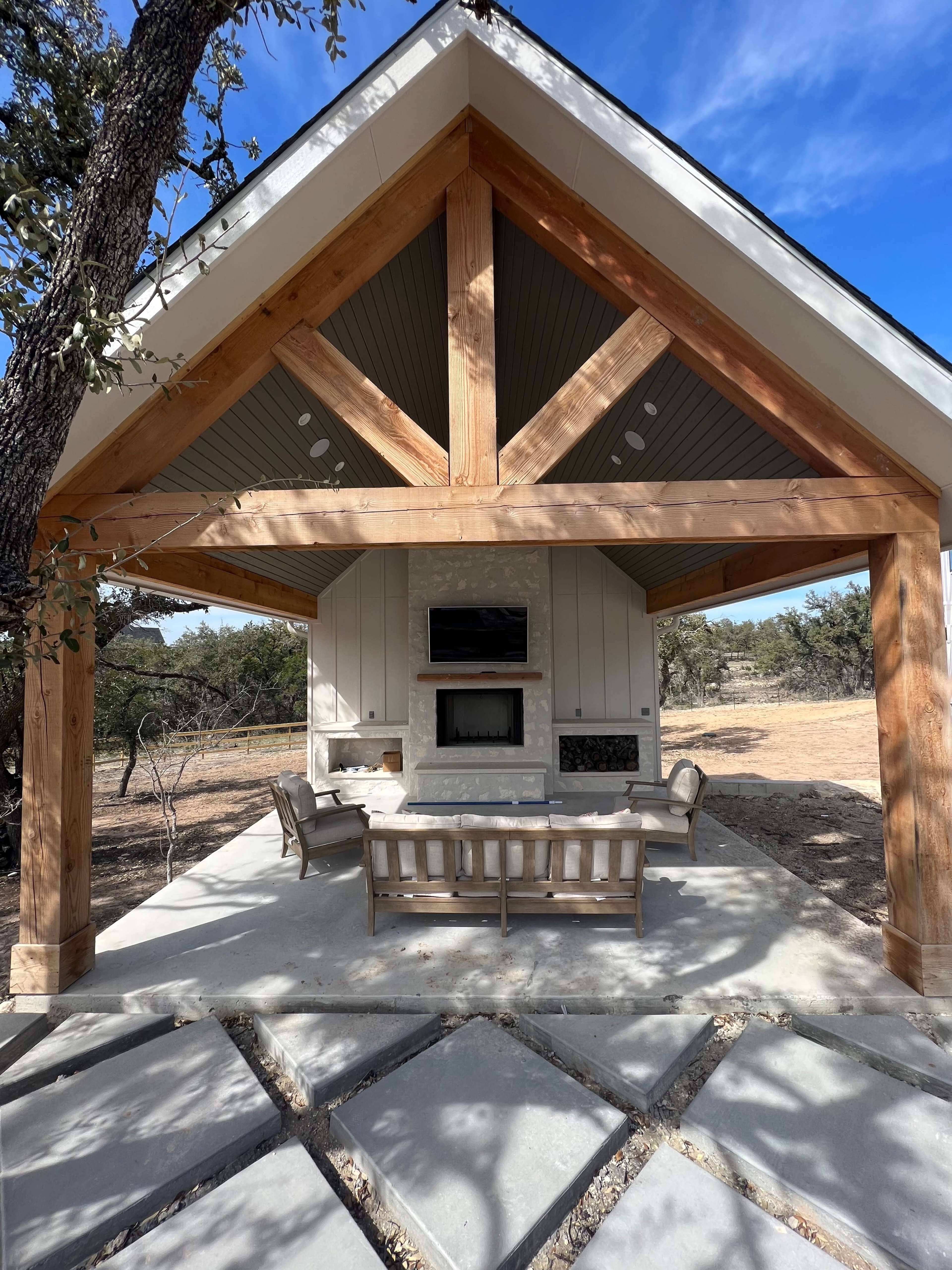 A modern outdoor patio with a wooden structure, featuring a stone pathway and a seating area beneath a gabled roof.