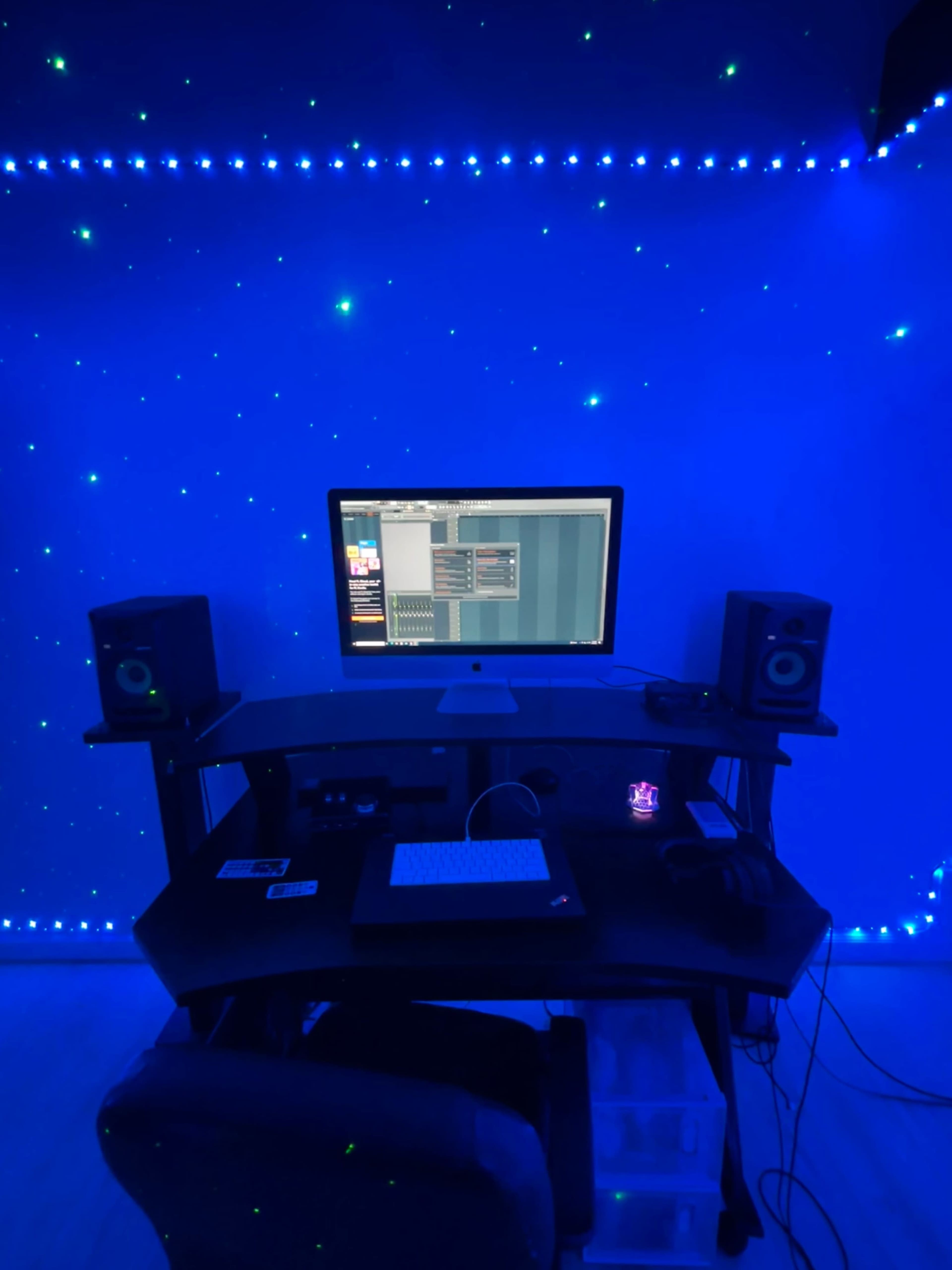 A computer workstation with speakers is set against a blue wall adorned with star-like lights.