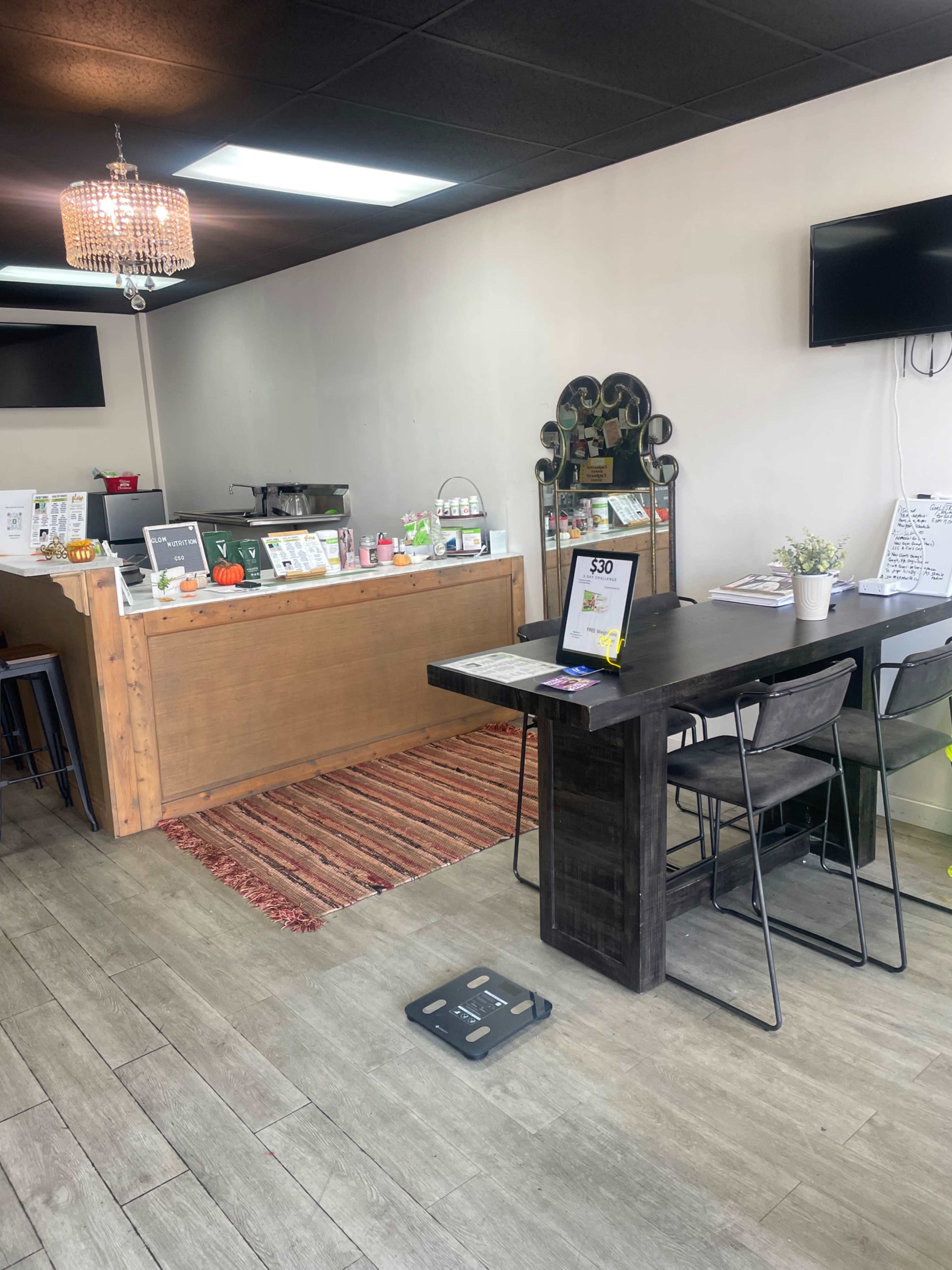 The image shows a modern service space with a wooden counter, tables, and chairs, along with decorative items and a digital screen on the wall.