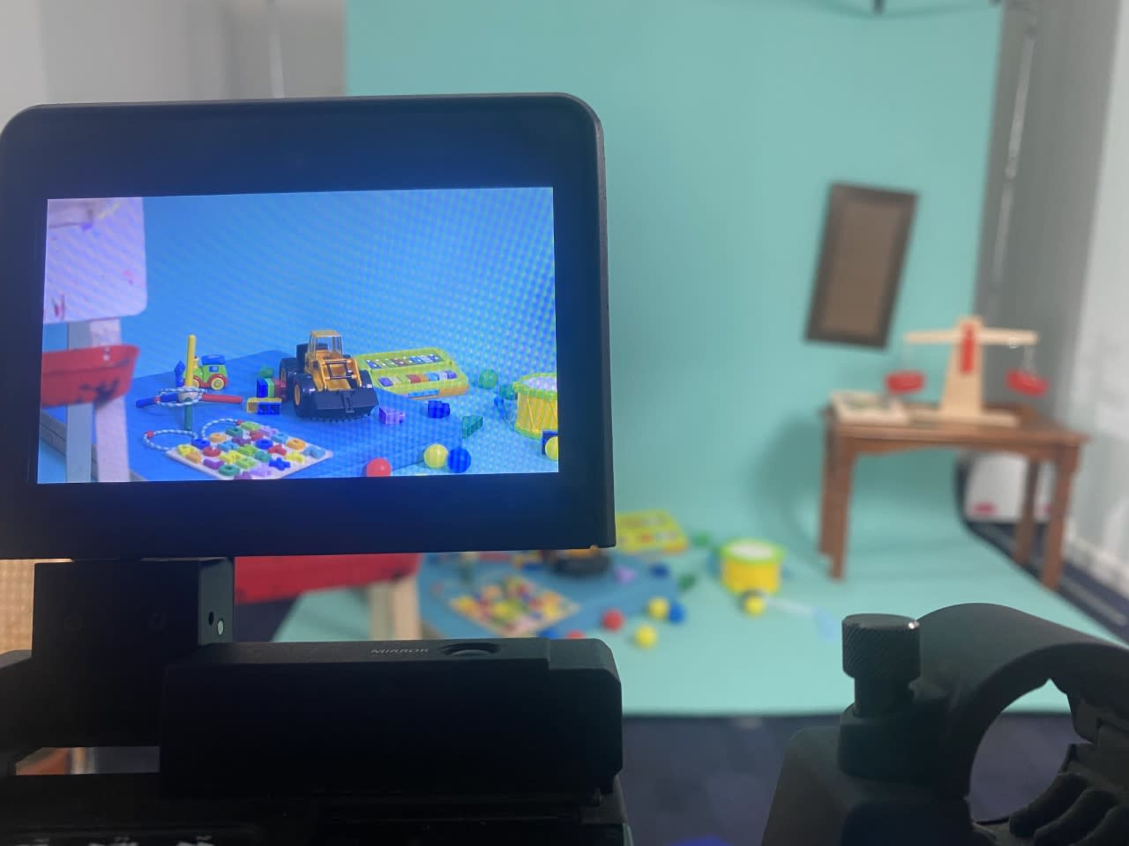 A camera viewfinder displaying a colorful arrangement of toys and play materials in a studio setup with a light blue background.