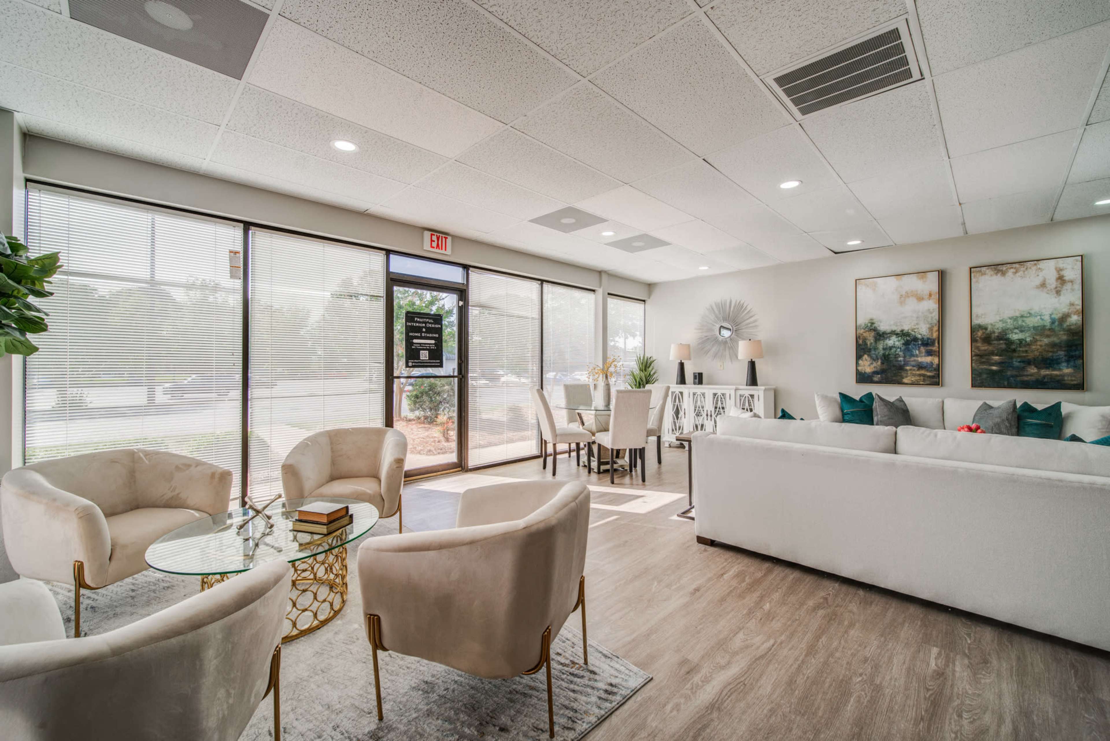The image shows a modern reception area with white furniture, plants, and large windows letting in natural light.