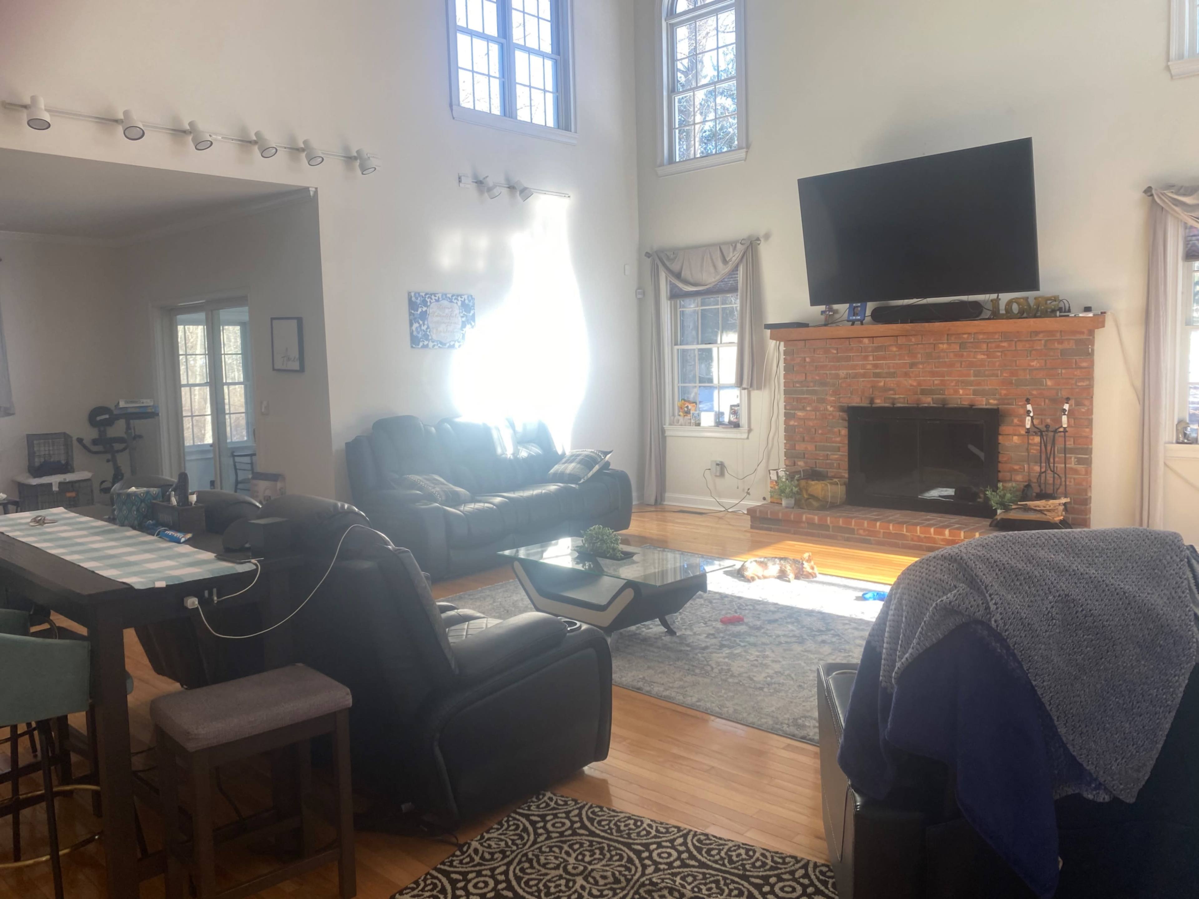 A spacious living room features leather sofas, a coffee table, and a brick fireplace with a large television mounted above it.
