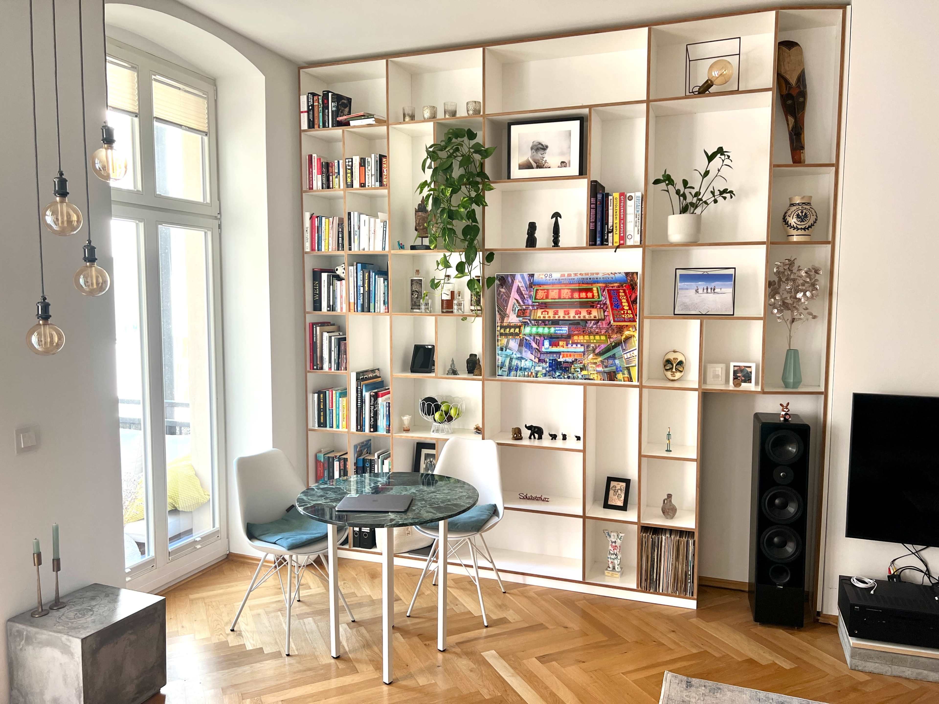 A modern living space featuring a bookshelf with an assortment of books and decorative items, a round table with two chairs, and a television on one side of the room.