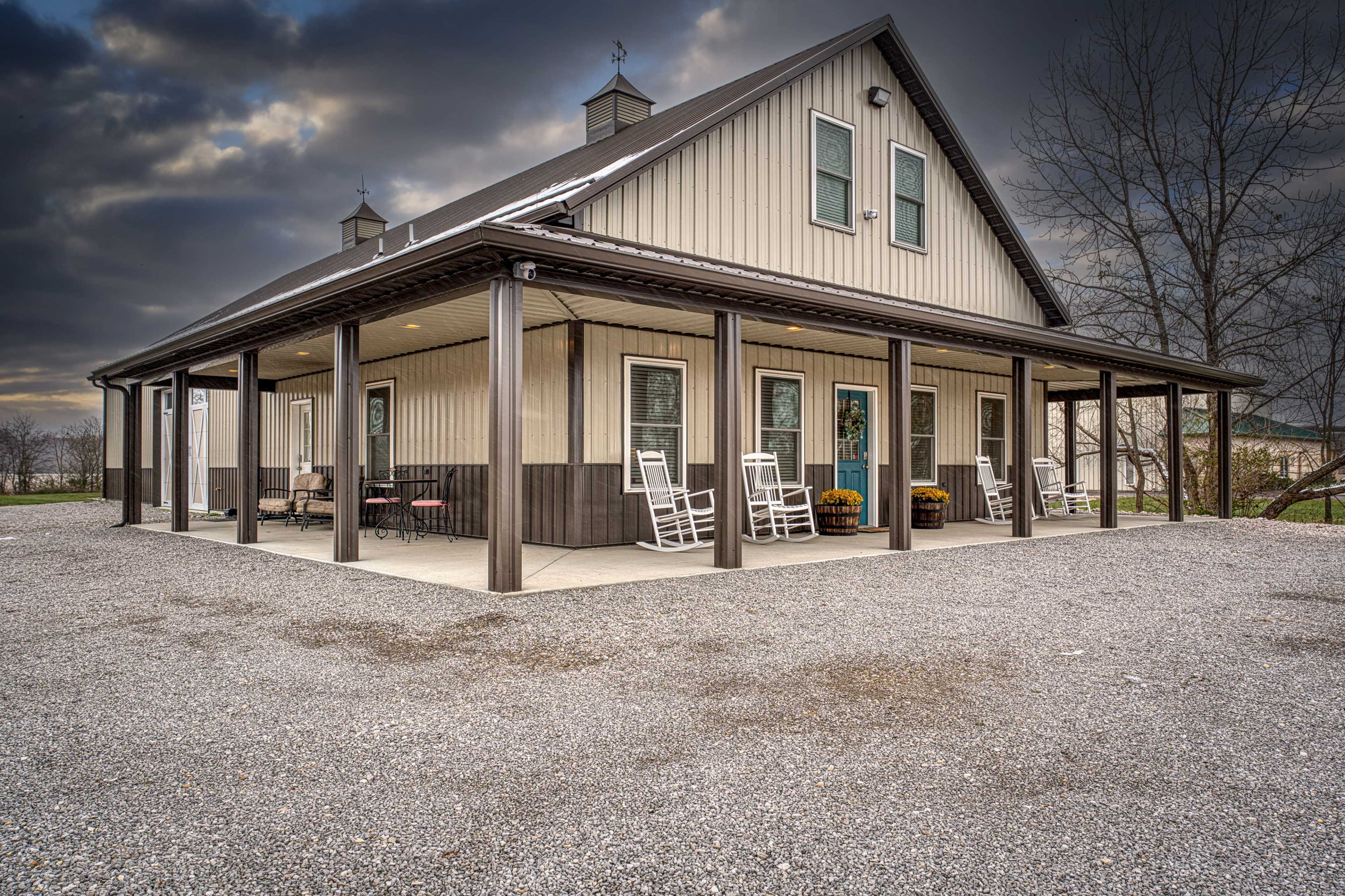 A large, modern house with a covered porch, rocking chairs, and gravel surrounding it, sits under a cloudy sky.