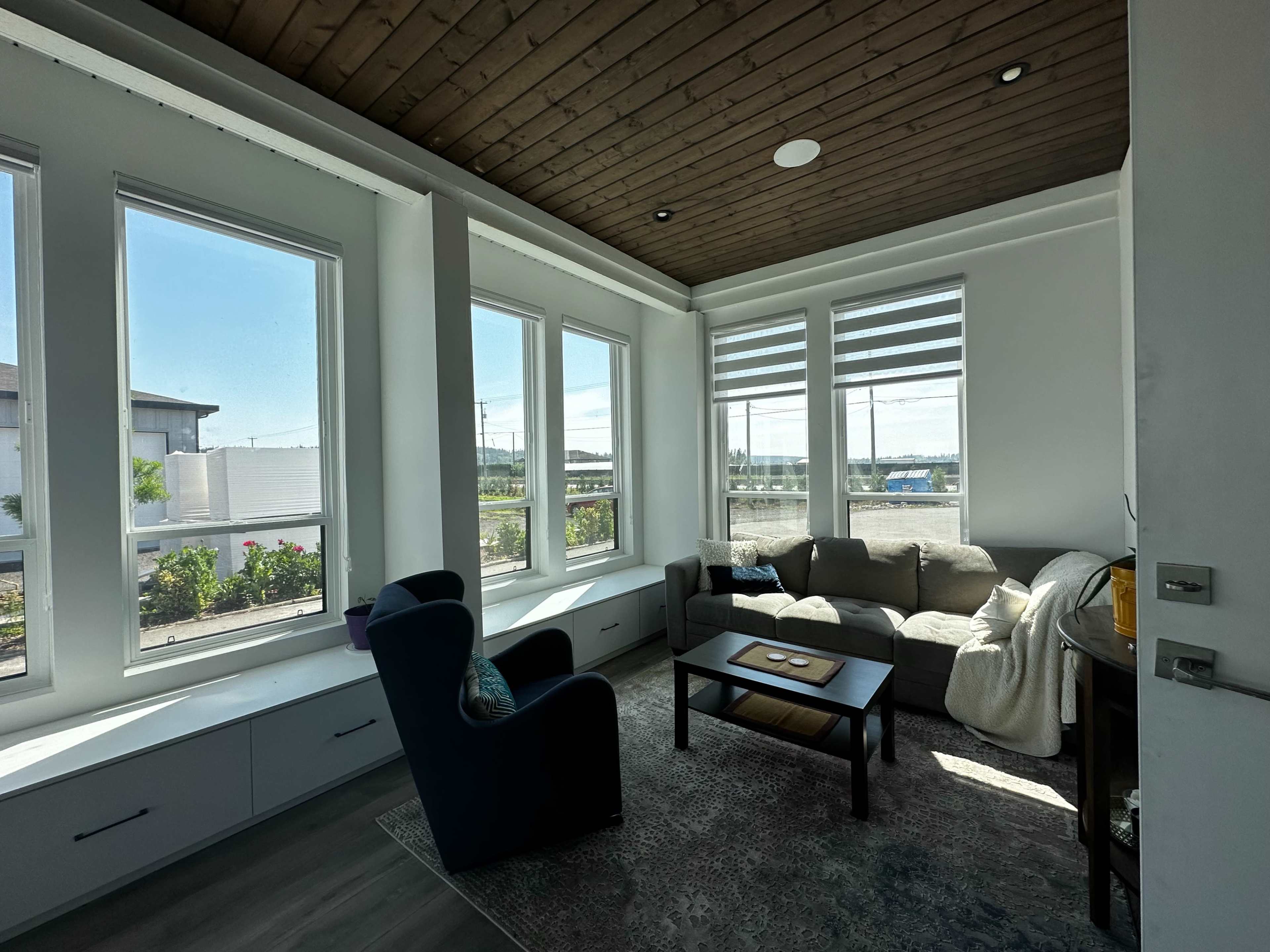 A bright living space with large windows, a gray sofa, a blue armchair, and a small coffee table.