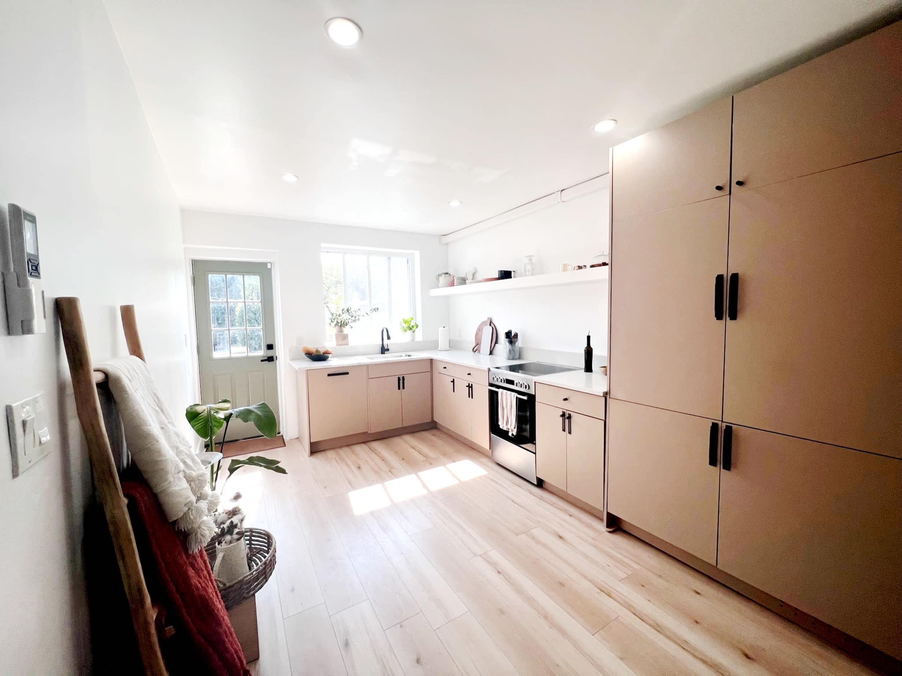 A modern kitchen features light cabinetry, a stainless steel oven, and a window overlooking a garden.