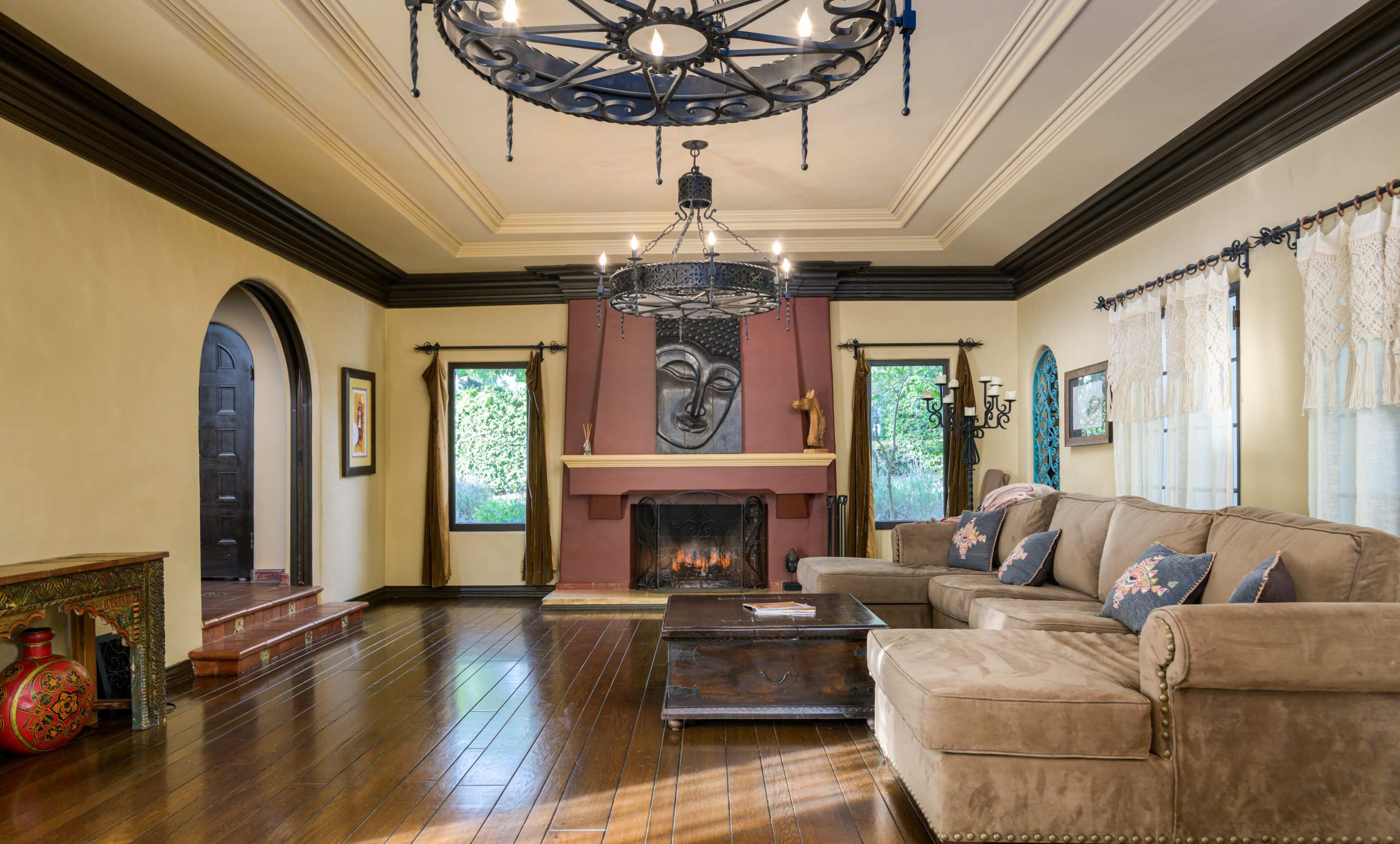 The living room features a cozy seating area with a large sofa, a mantelpiece adorned with an artistic face plaque, and hardwood floors illuminated by a chandelier.