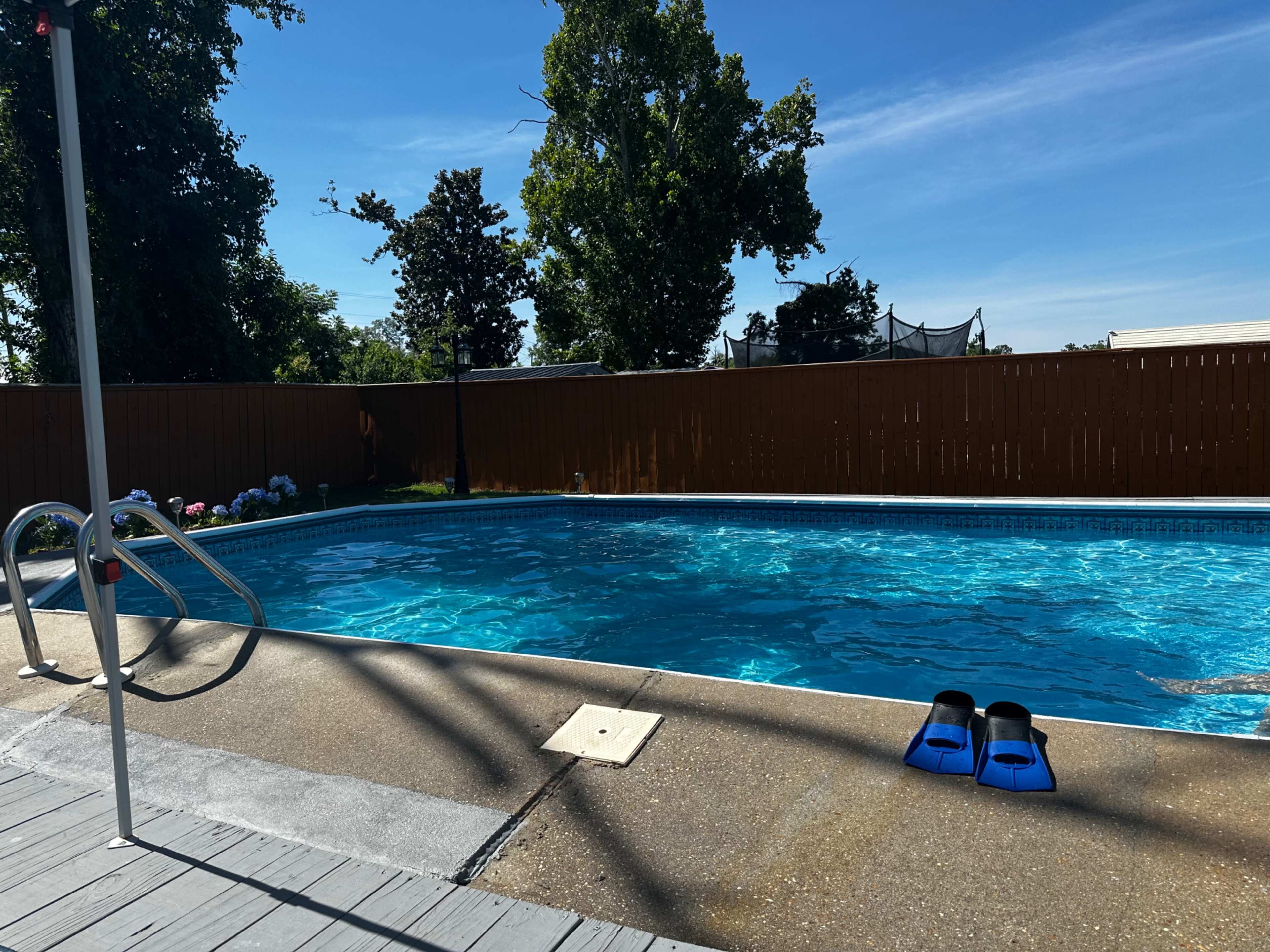 A swimming pool is surrounded by a wooden fence with blue swimming fins placed on the edge of the concrete deck.