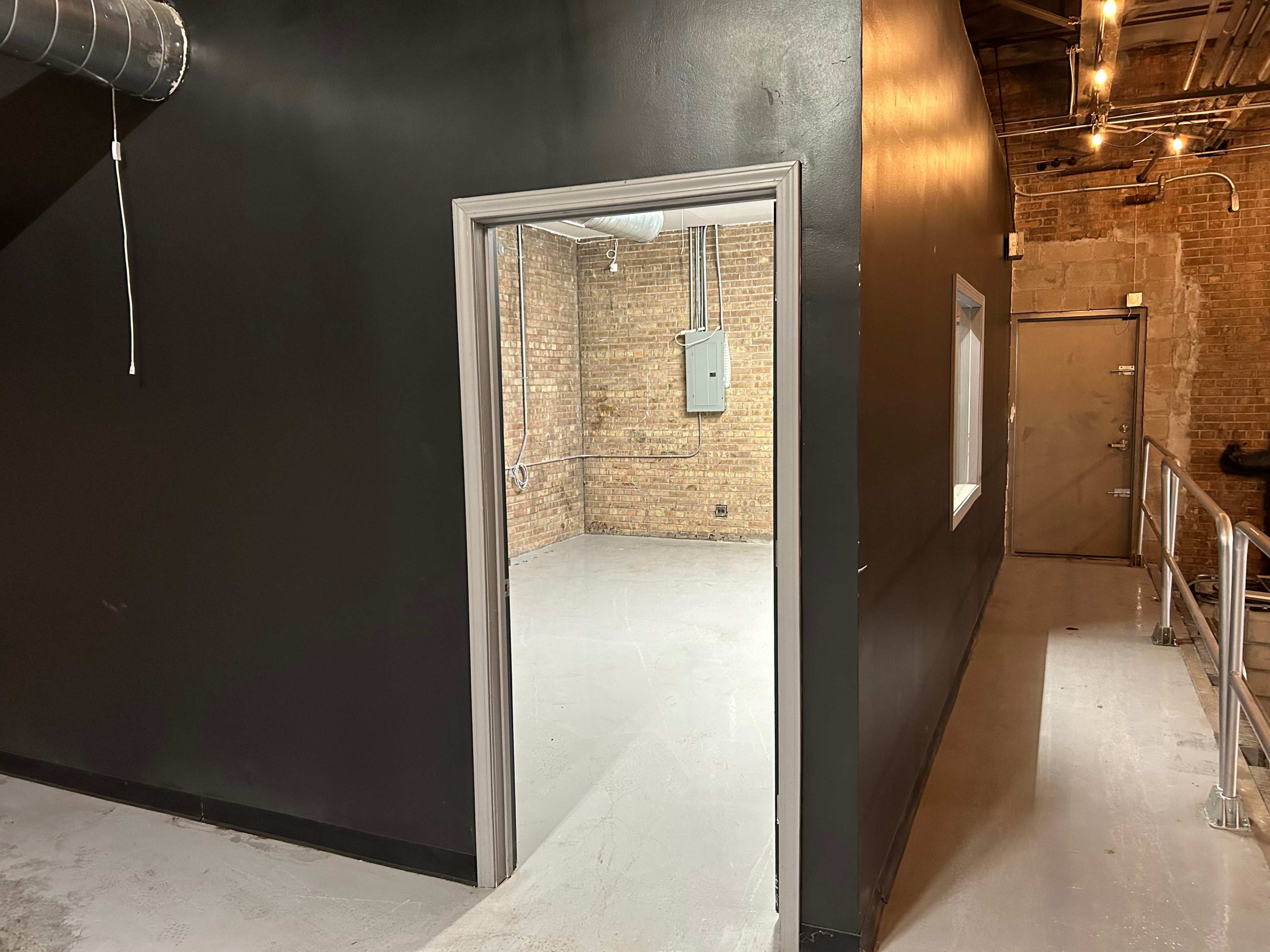 A doorway leading from a black-painted wall into a room with exposed brick walls and a concrete floor.