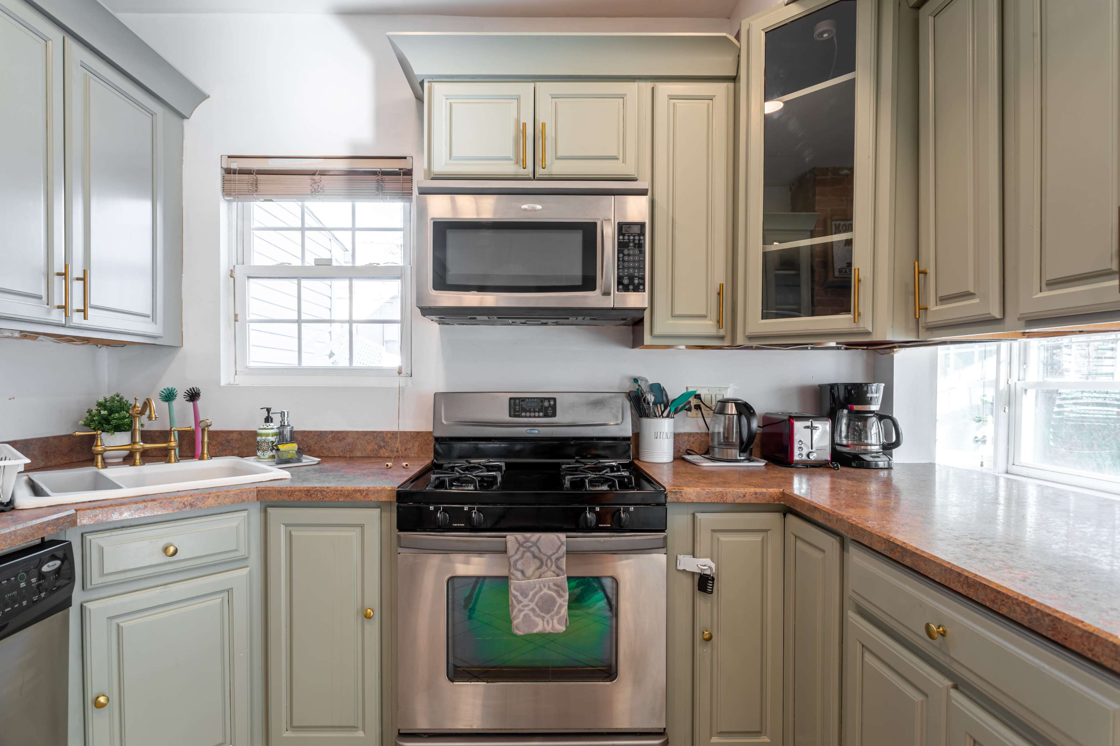 A kitchen with light green cabinets, a stainless steel stove, and various kitchen appliances on the counter.