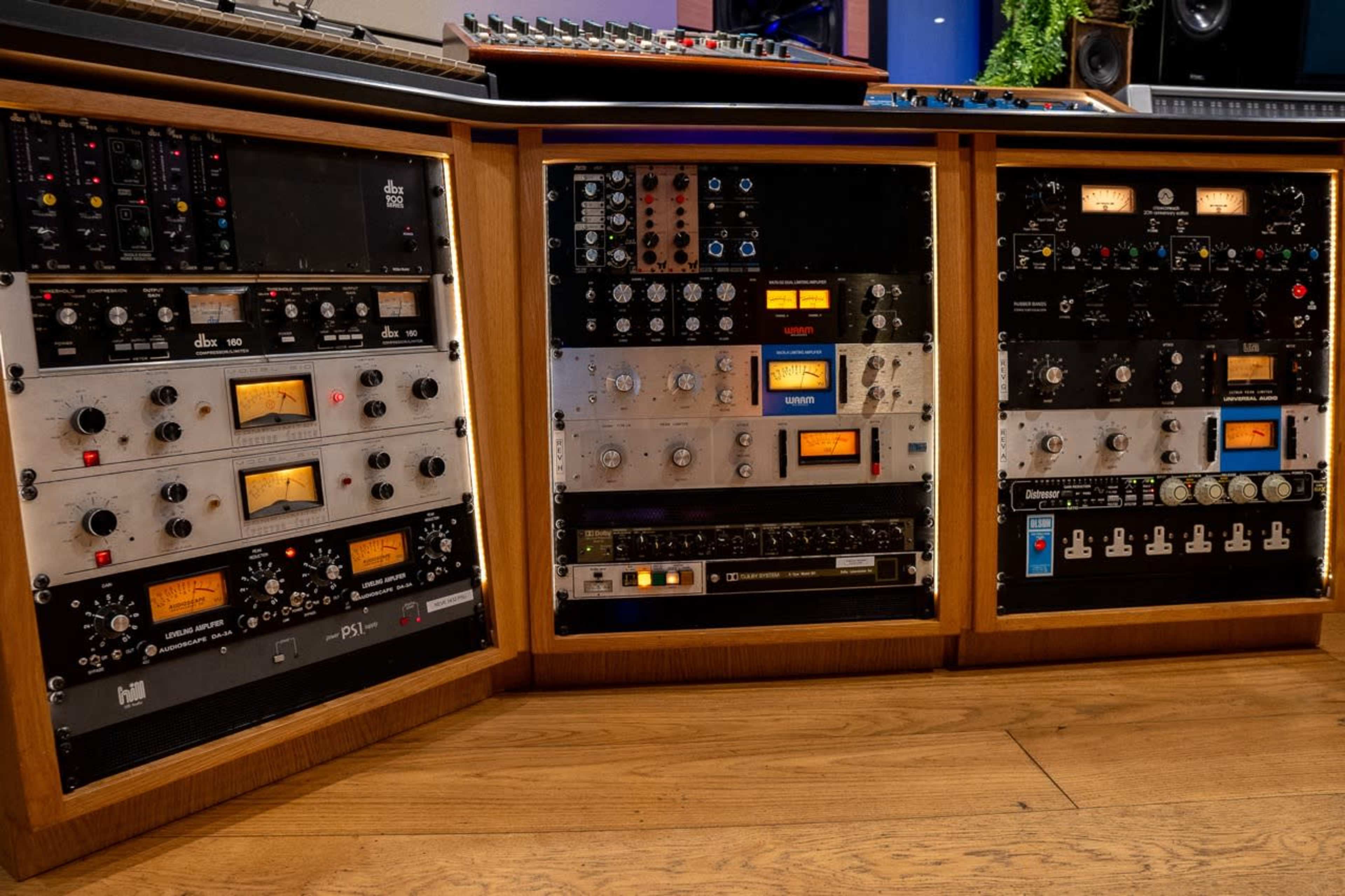 The image shows a wooden studio console featuring multiple audio equipment racks filled with various audio processing devices and meters.