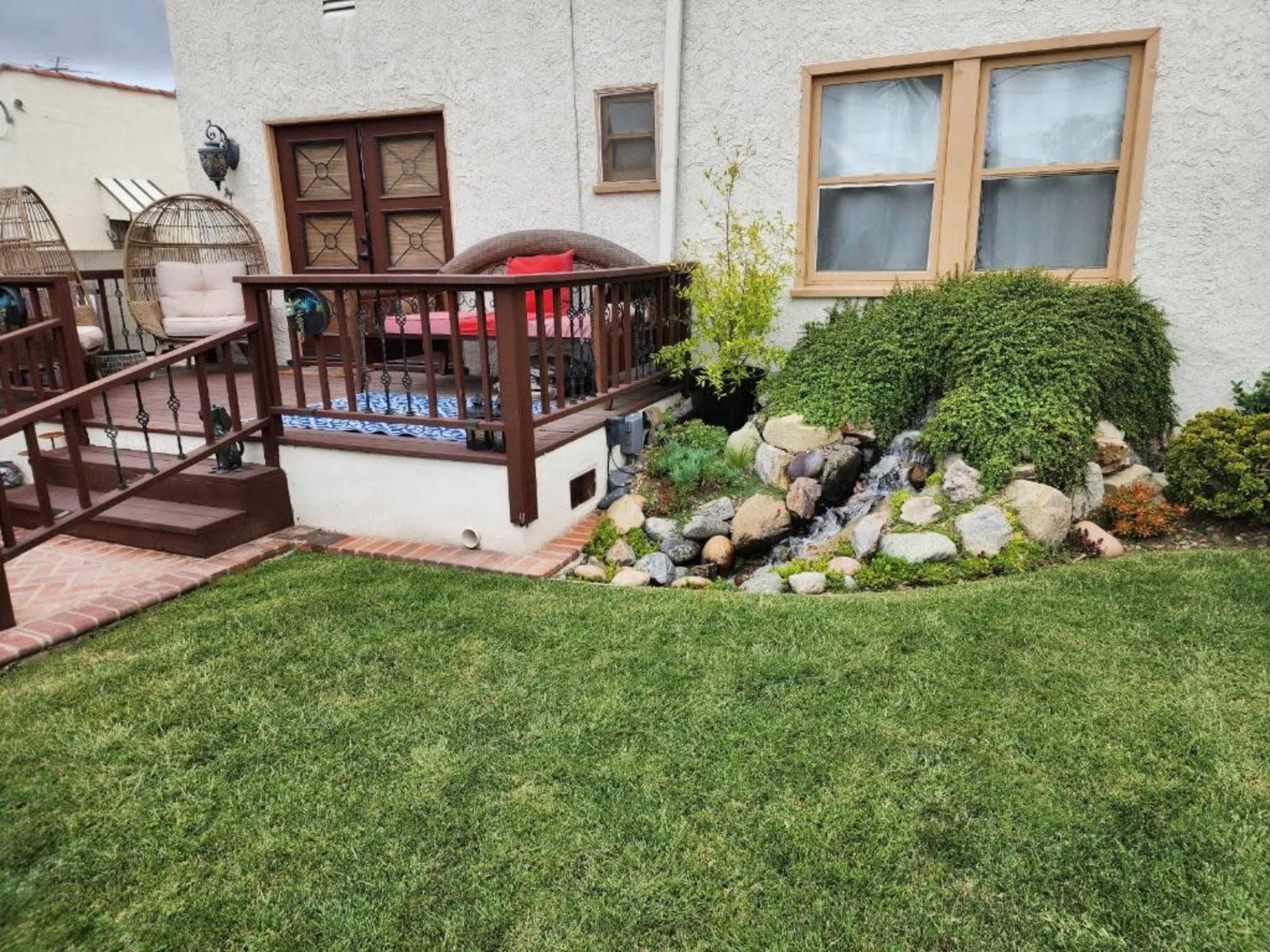 A landscaped backyard with a garden area featuring rocks, a small water feature, and a wooden deck with seating.