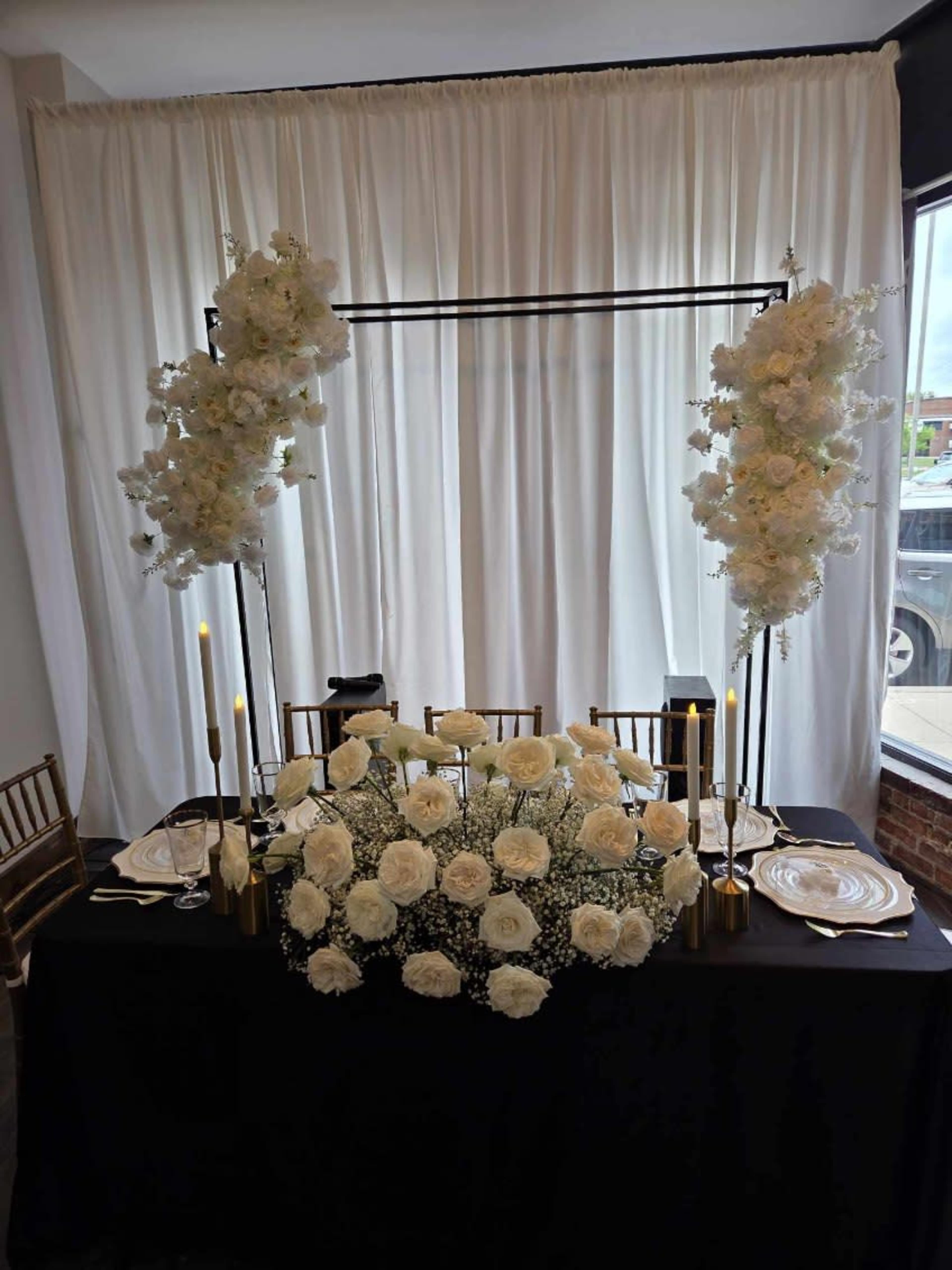 A decorated table with white flowers and candles is set against a backdrop of sheer white fabric.