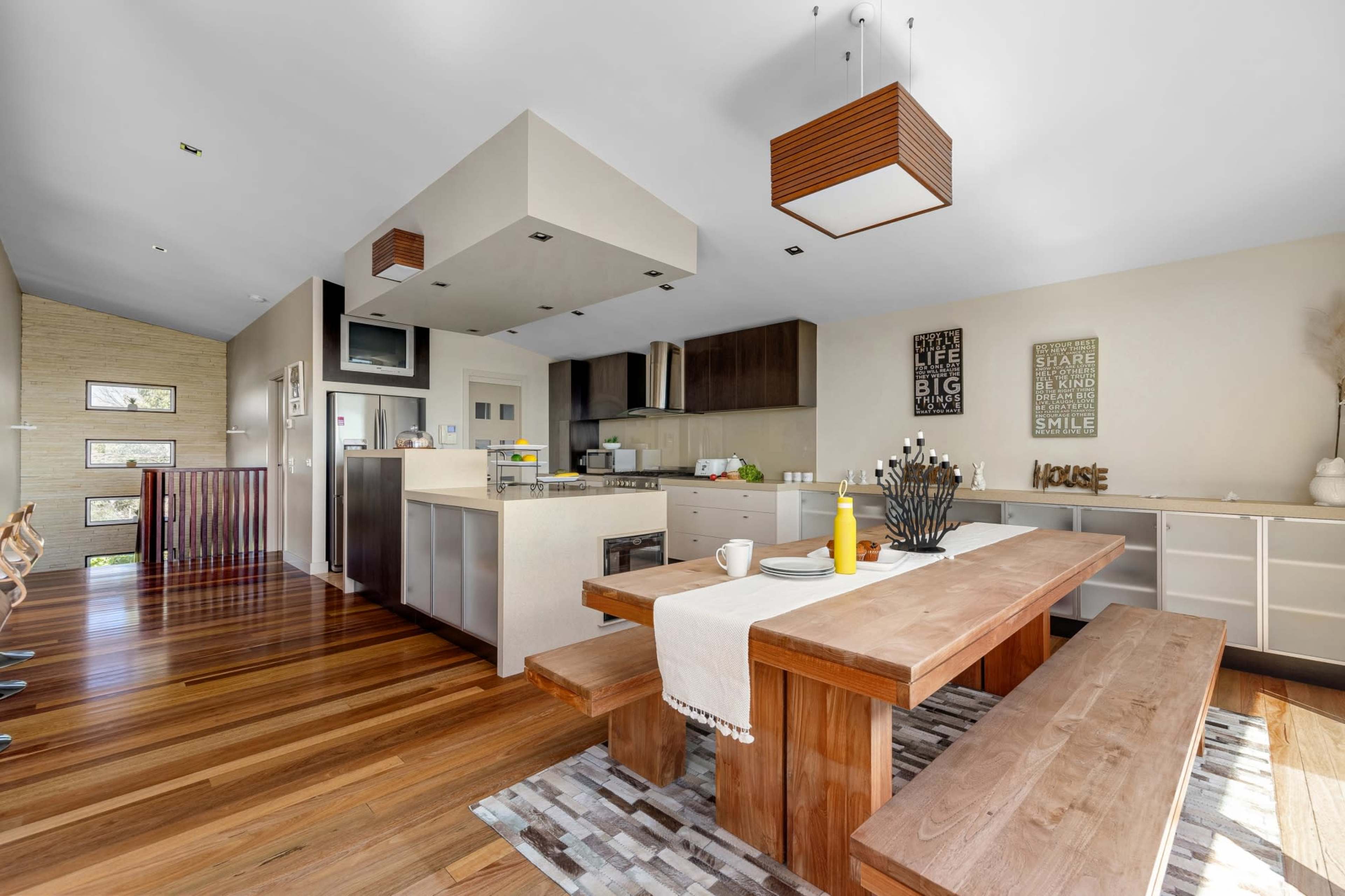 The image depicts a modern kitchen and dining area with a large wooden table, bench seating, and contemporary cabinetry.