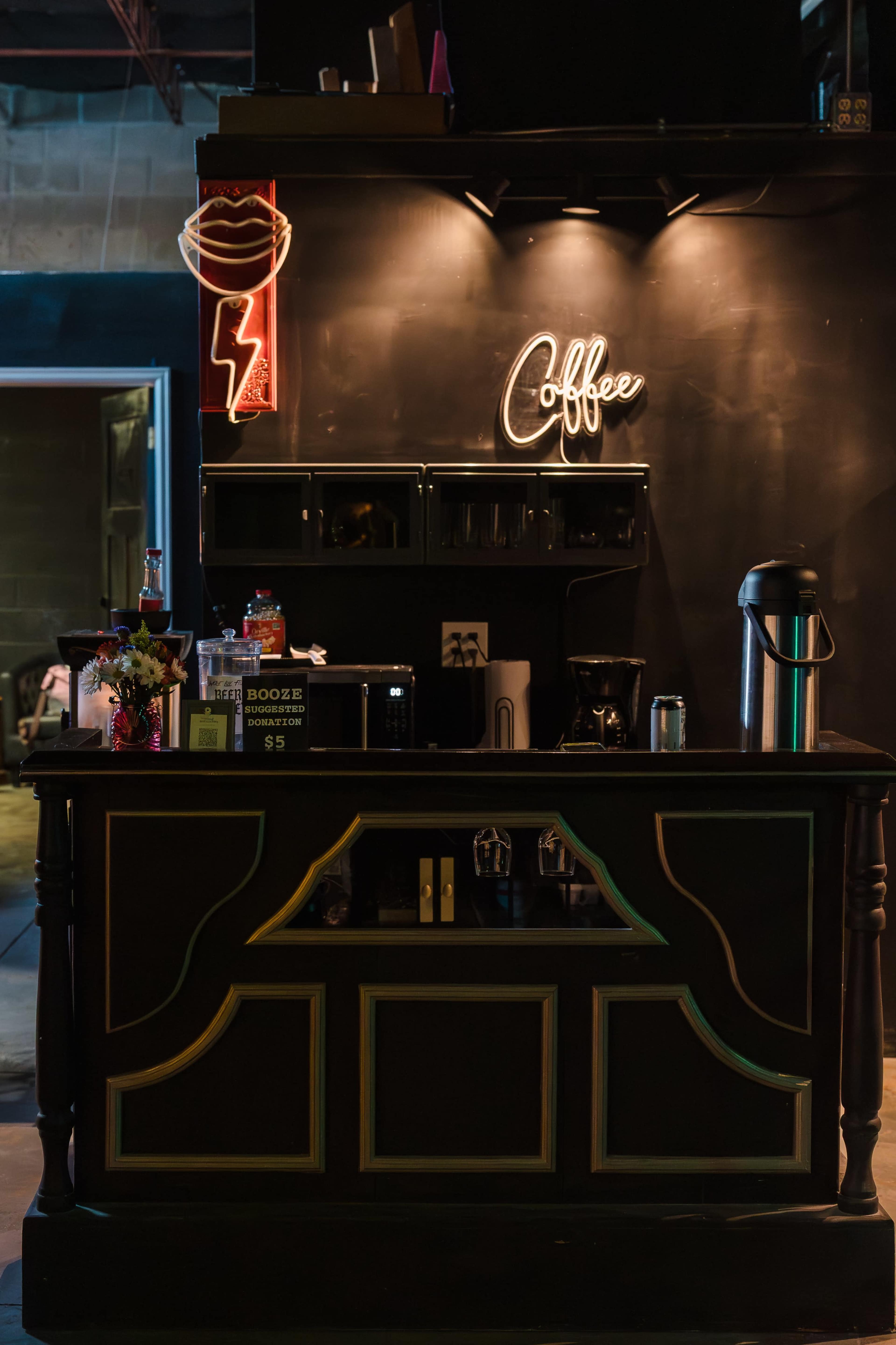 The image shows a coffee bar with a wooden counter featuring a neon sign that reads "Coffee," set against a dark backdrop.