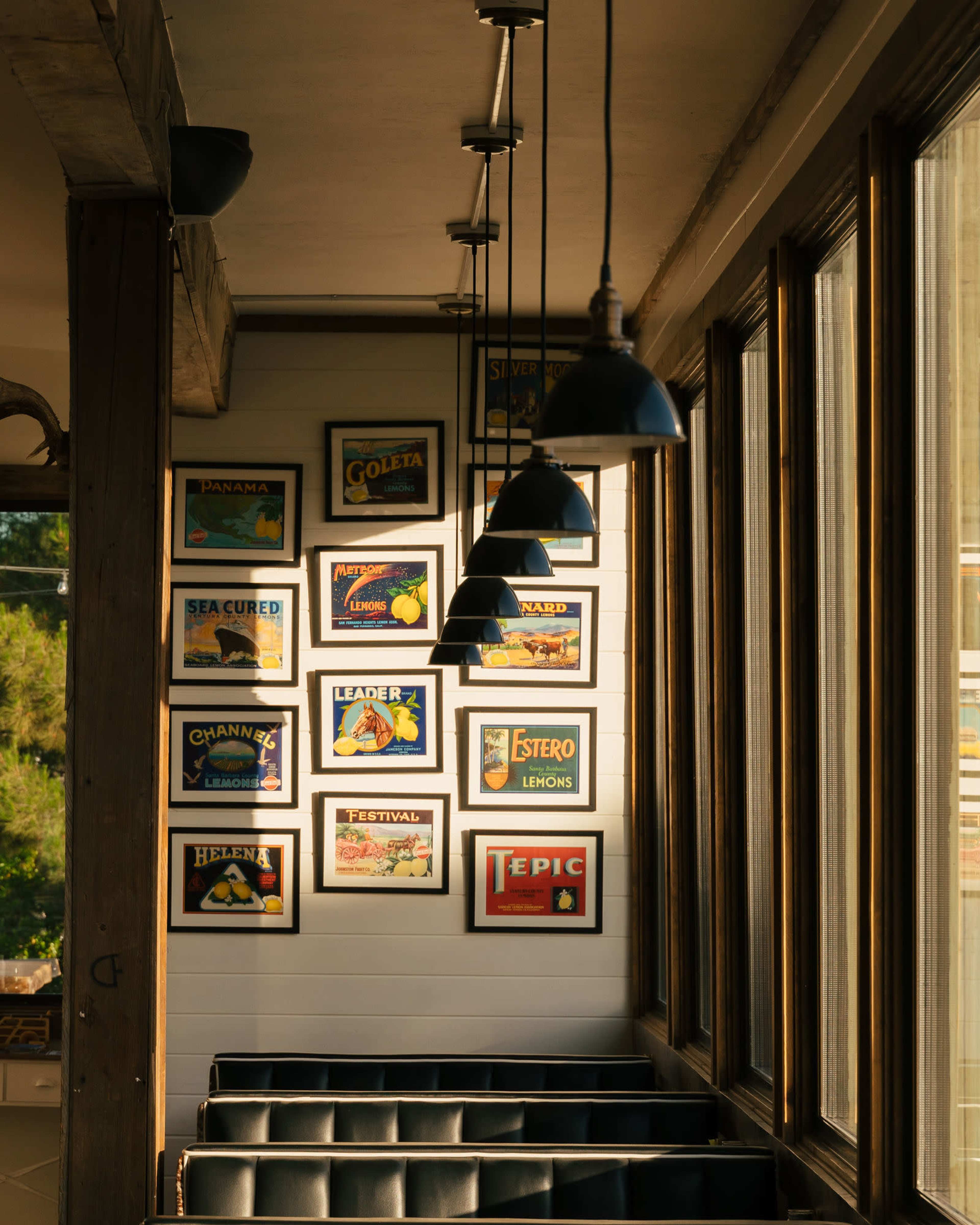 A well-lit interior space featuring framed posters on a wall, with pendant lamps hanging above a seating area.