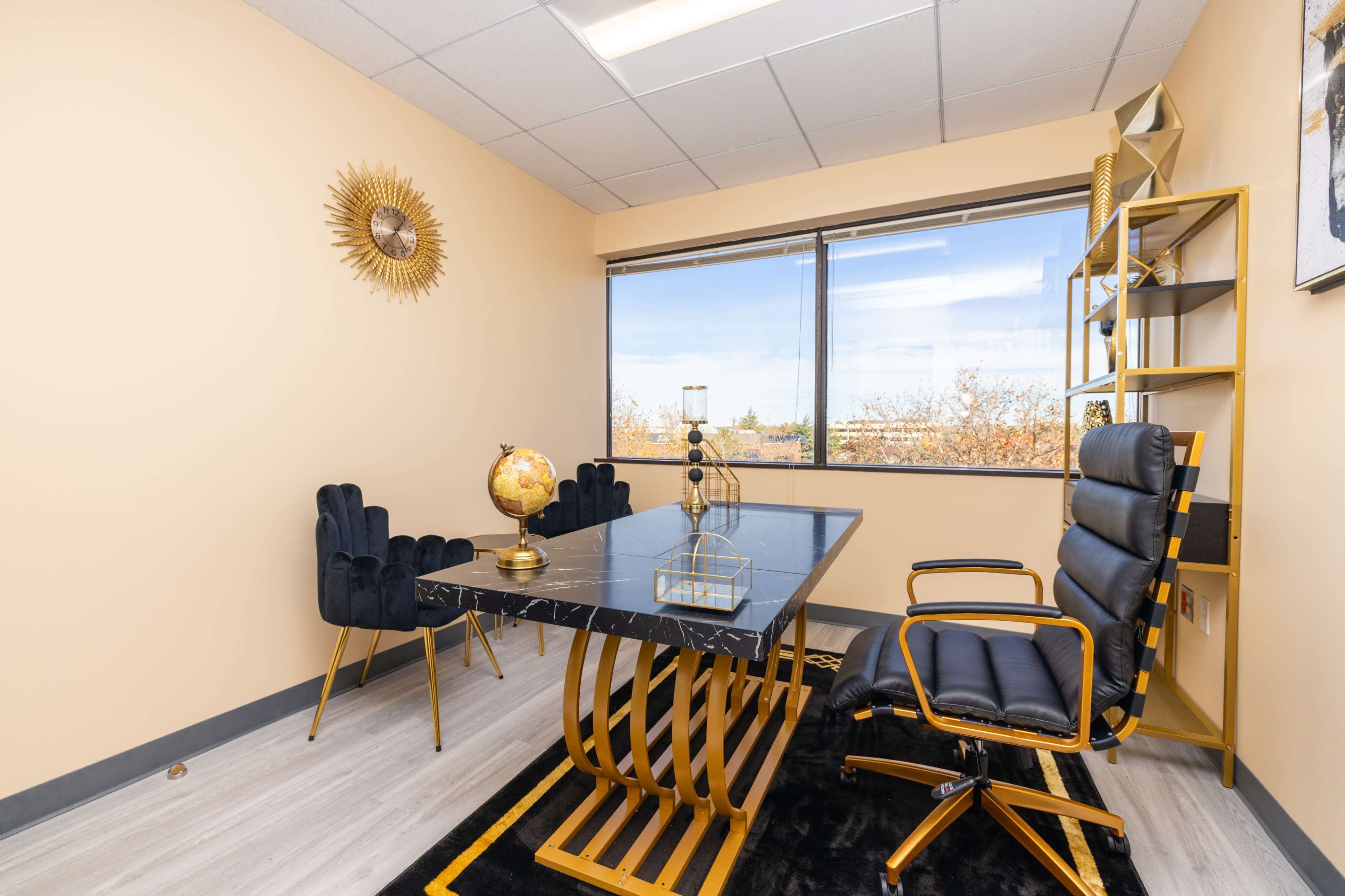 A modern office space featuring a black marble table, a black leather chair, two upholstered chairs, and a decorative globe, all set against a light-colored wall and large window.