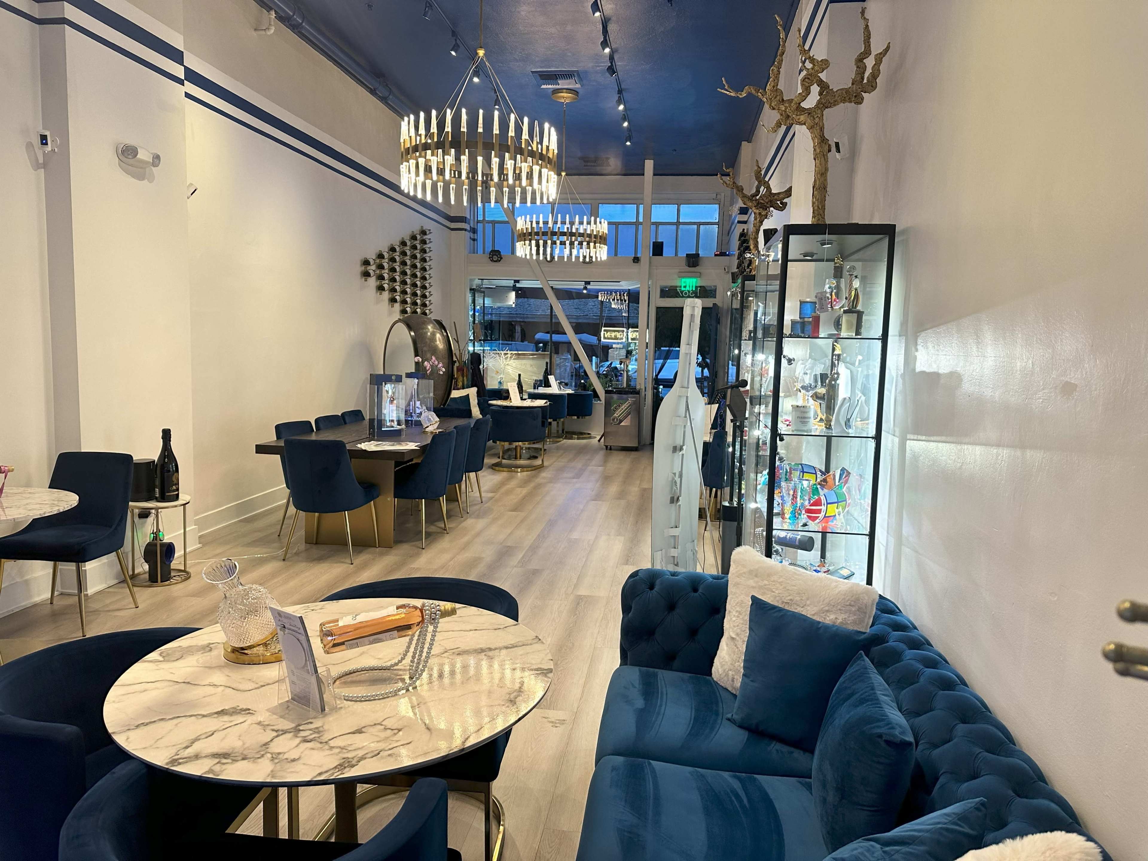 A modern interior of a stylish cafe featuring a blue and white color scheme, marble tabletops, and various seating areas.