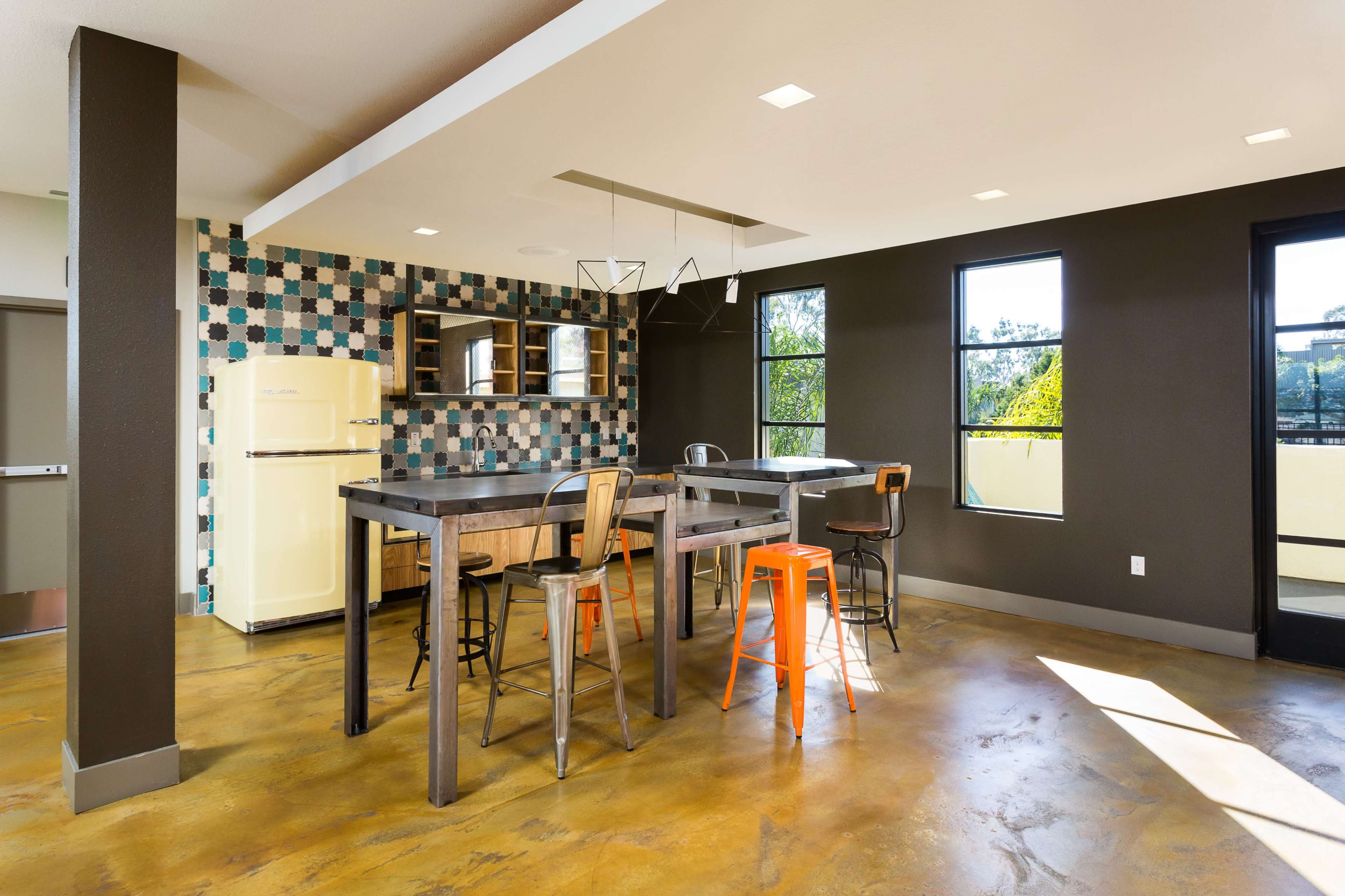 A modern kitchen features a table with metal and wooden stools, an orange bar stool, and a vintage refrigerator against a patterned tiled wall.