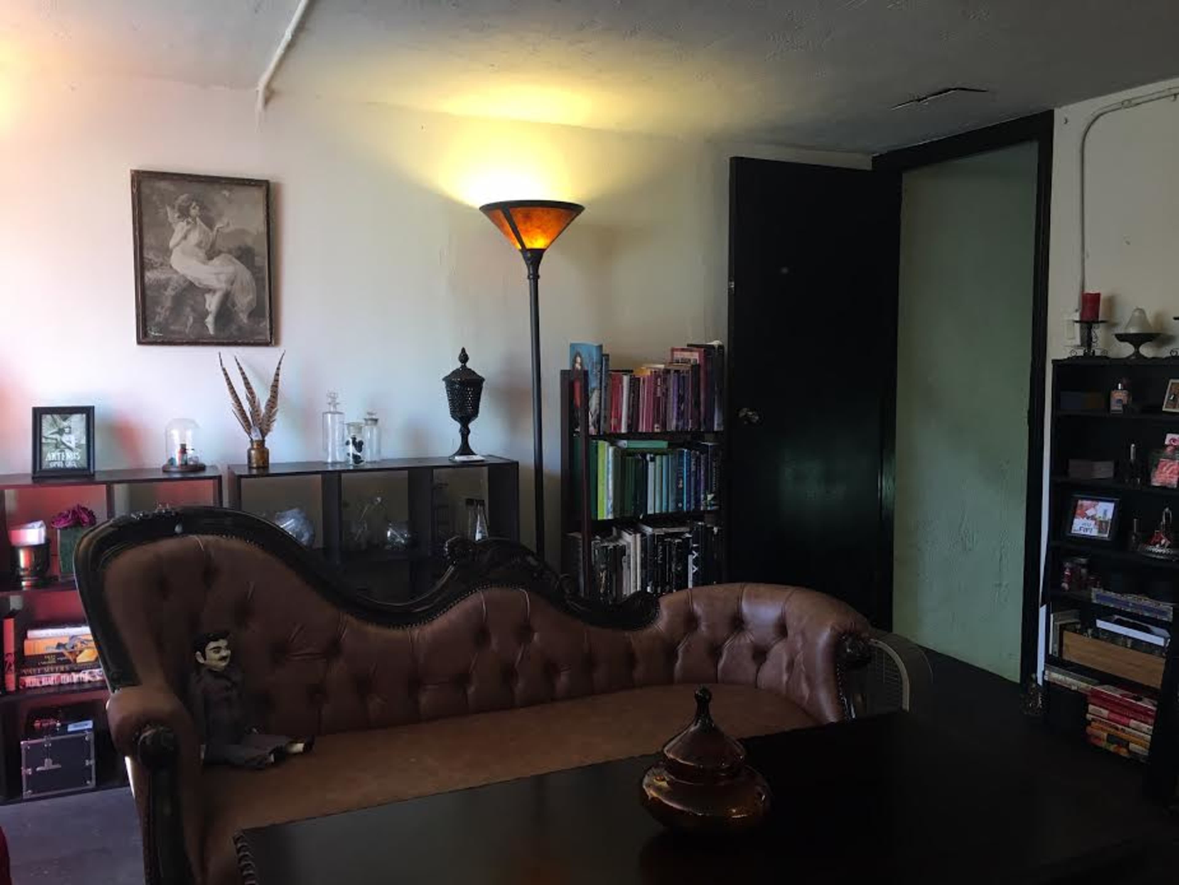 A cozy living room featuring a vintage couch, a lamp, a bookshelf, and a door leading to another room.