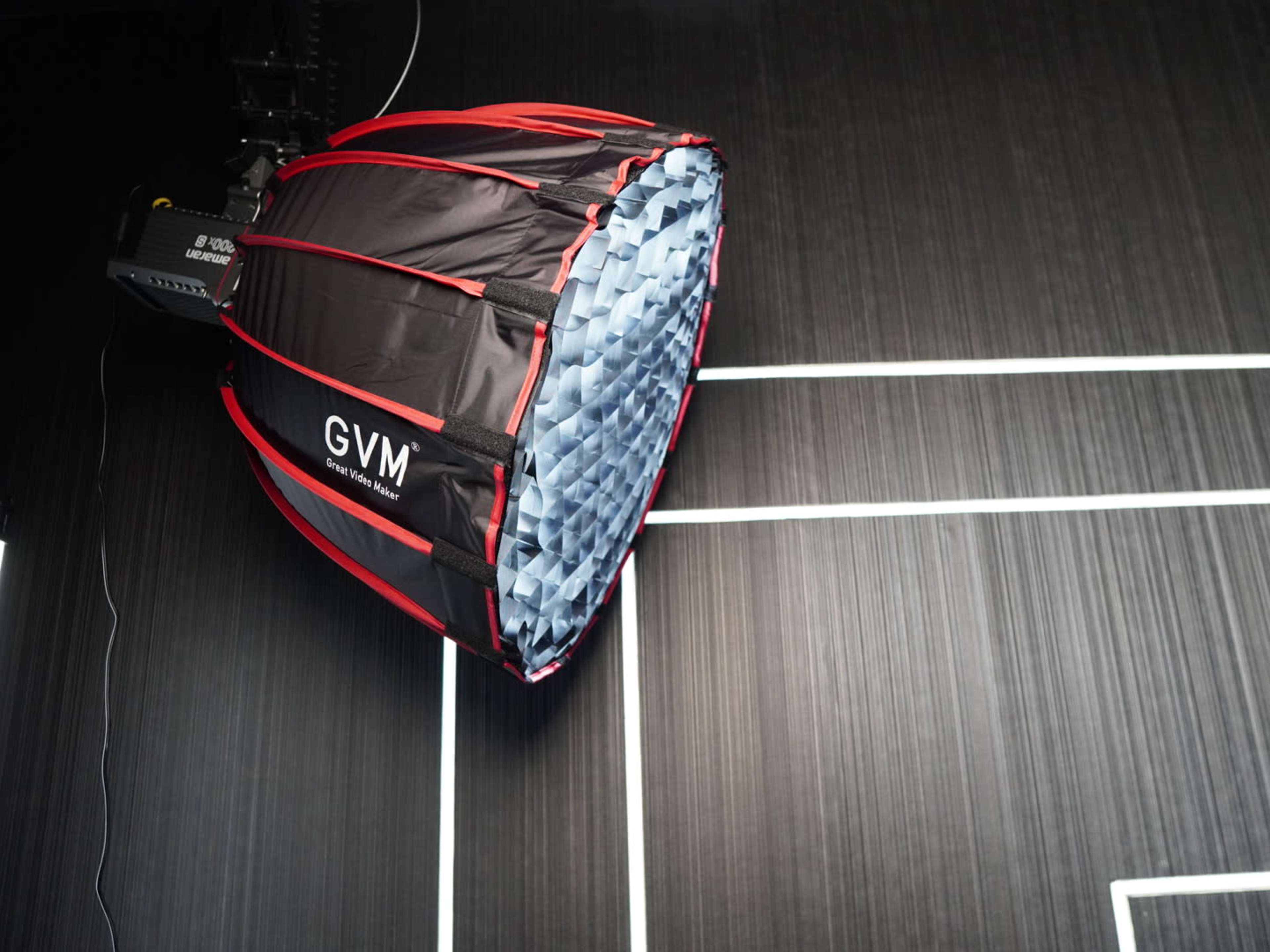 A large softbox light is mounted on the ceiling, casting light onto a textured black wall with white lines.