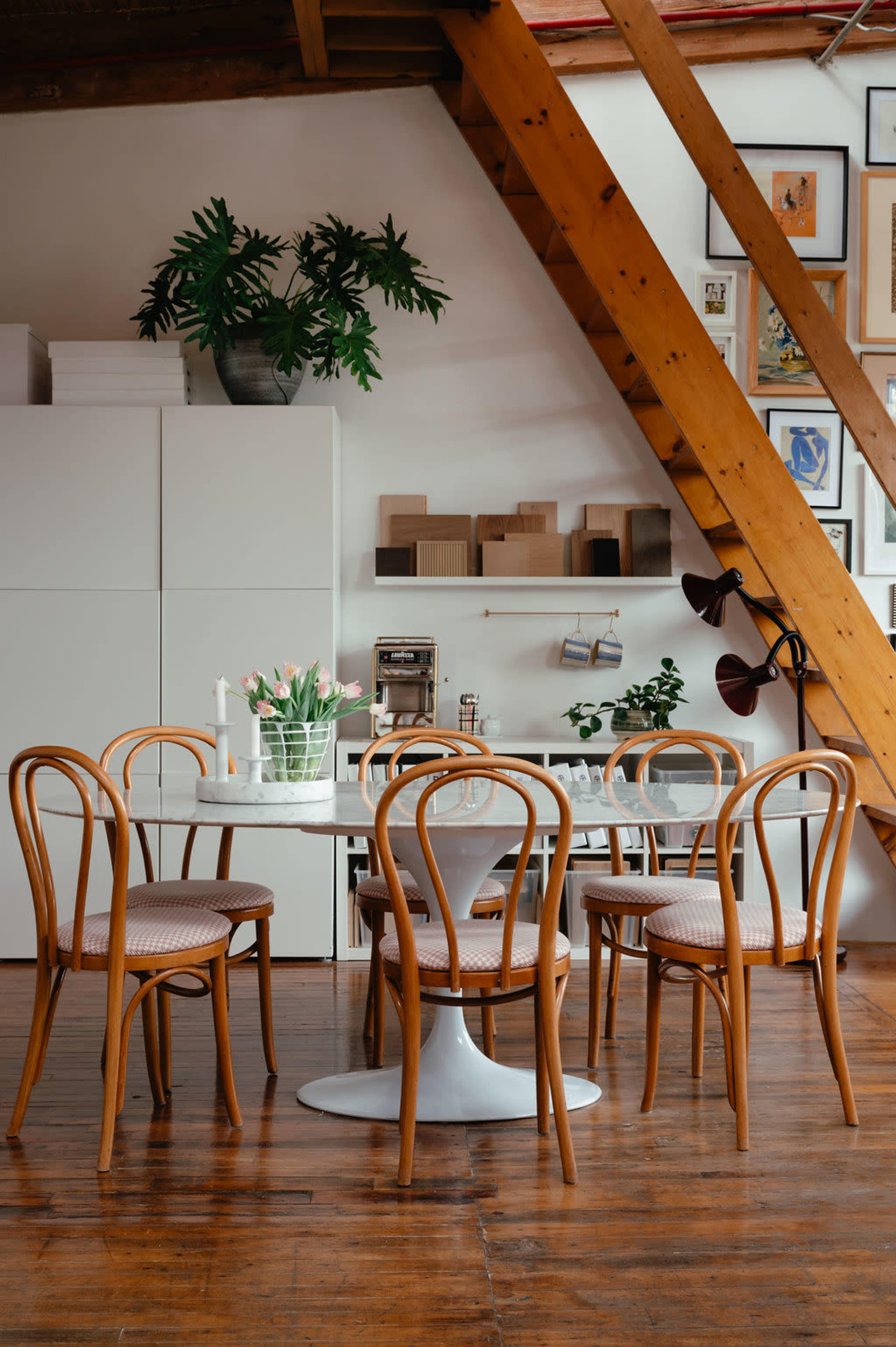 A stylish dining area features a round table with wooden chairs, surrounded by a mix of décor and artwork against a backdrop of wooden beams.