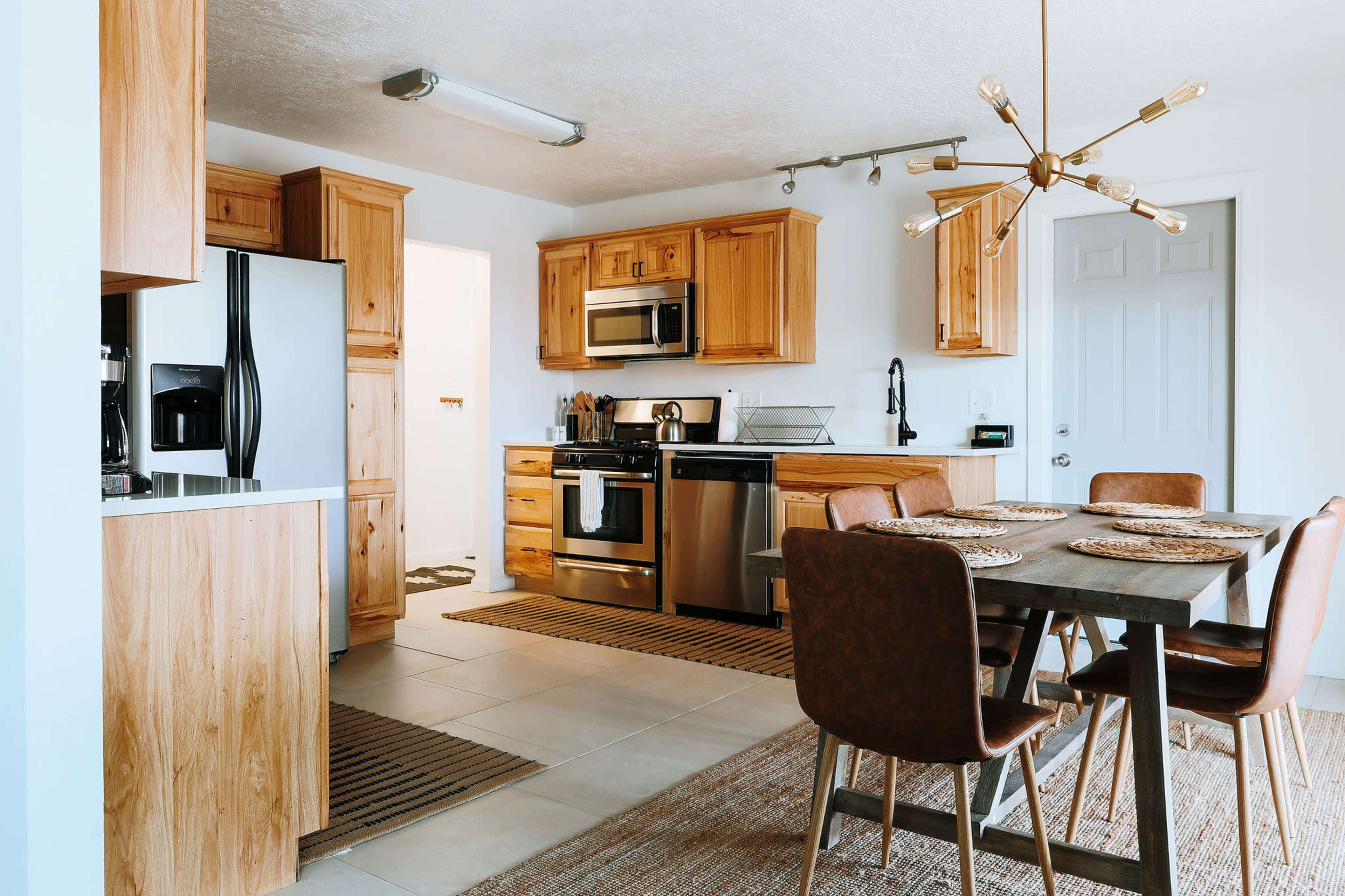 A modern kitchen with wooden cabinetry, stainless steel appliances, and a dining area featuring a table and upholstered chairs.