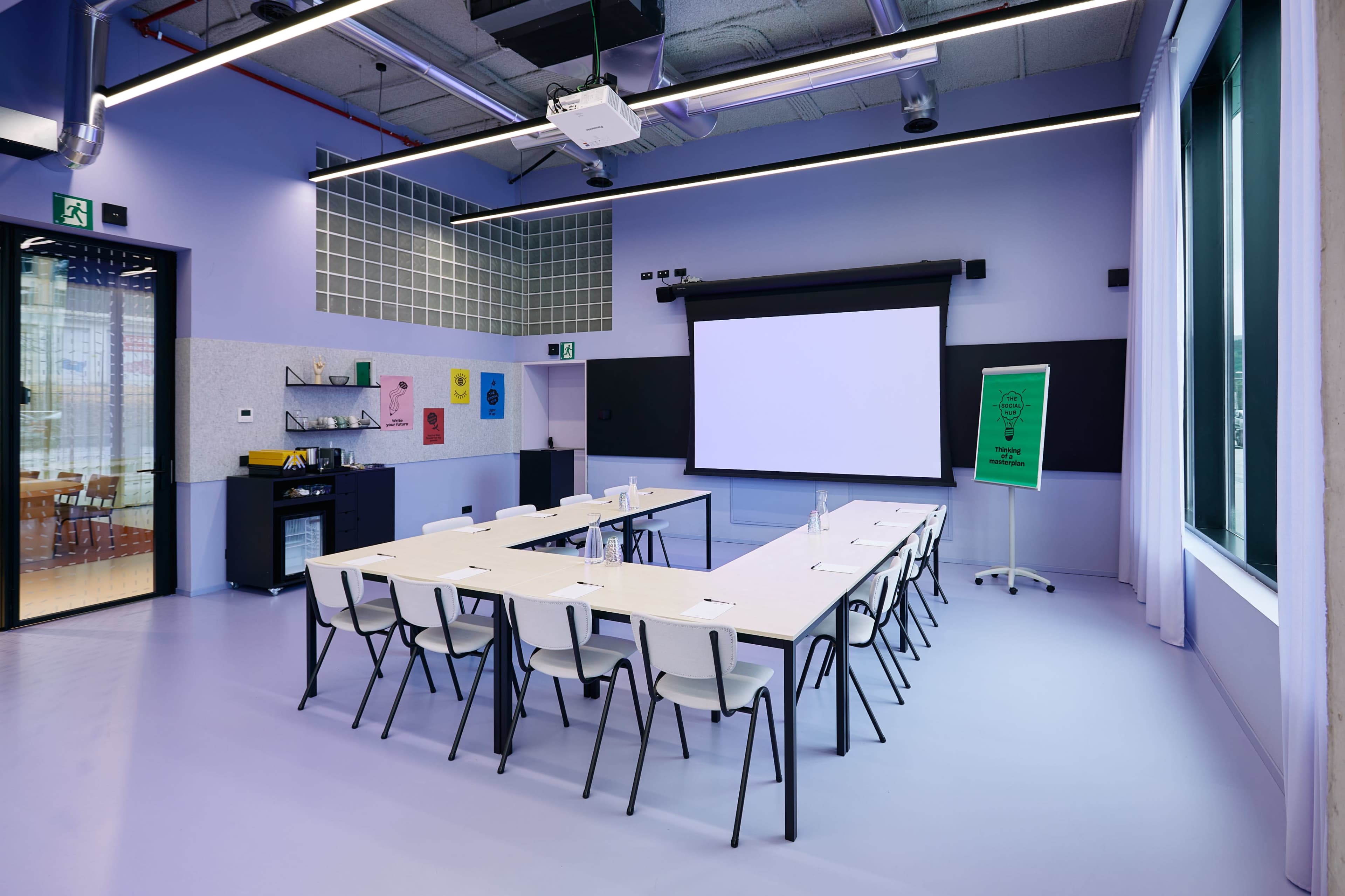 A modern conference room with a large projection screen, a long table set for a meeting, and colorful artwork on the walls.