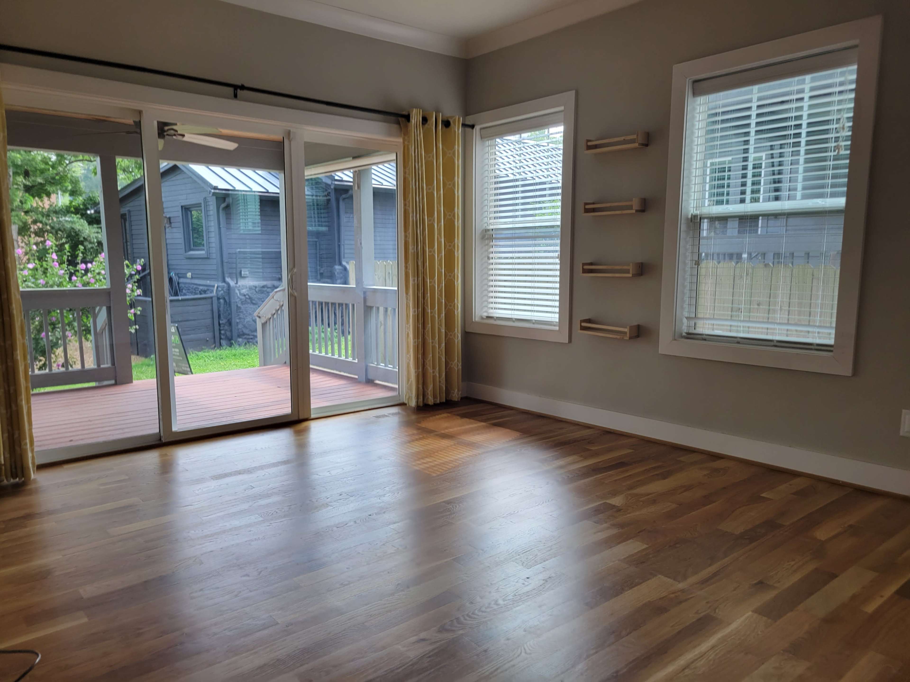 The room features hardwood floors, large windows with yellow curtains, and a sliding door that opens to a wooden deck.