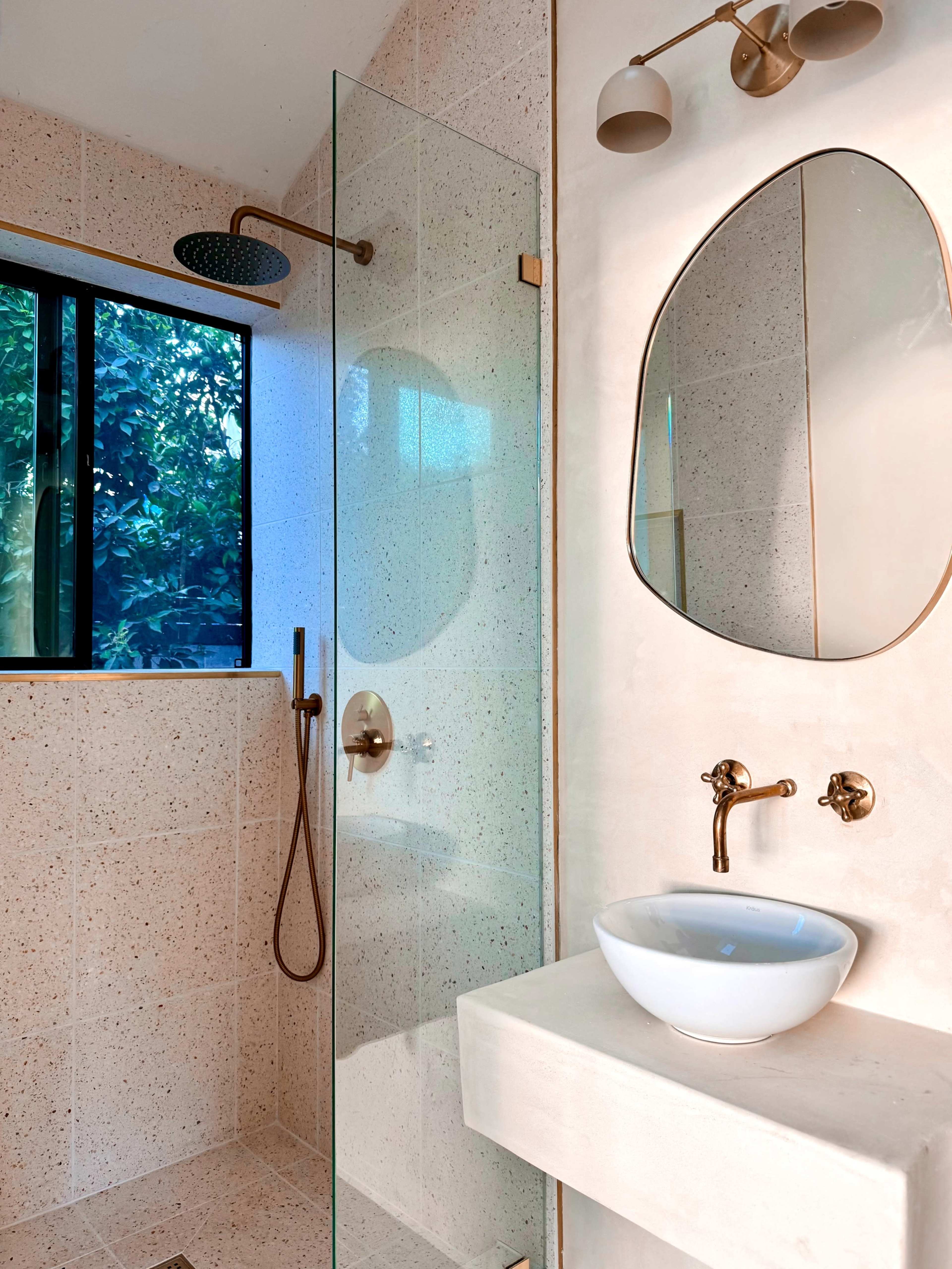 The image shows a modern bathroom featuring a glass shower enclosure, a wall-mounted mirror, and a vessel sink on a stone countertop.