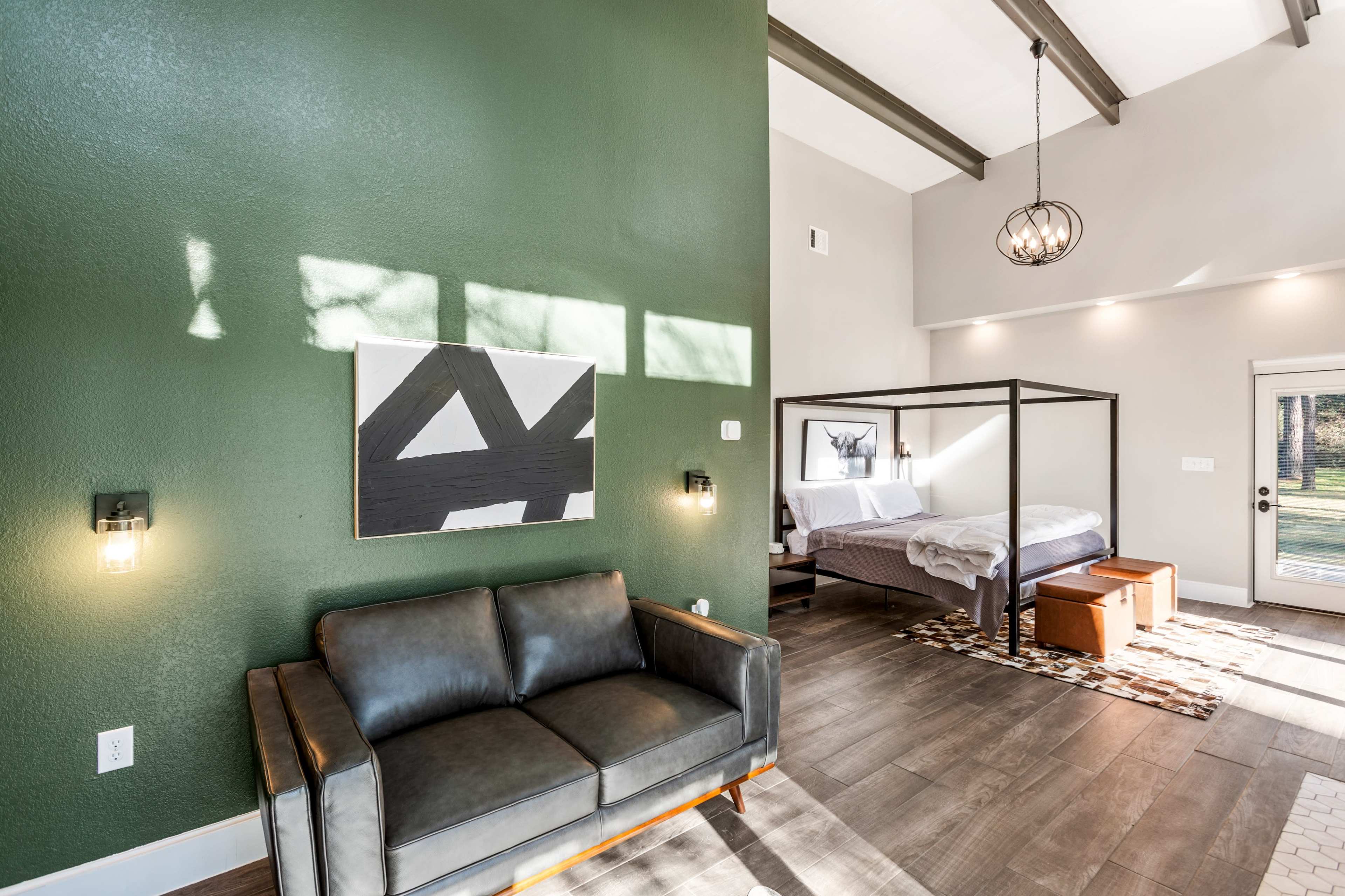 A modern interior space with a green accent wall, a four-poster bed, and a leather sofa.