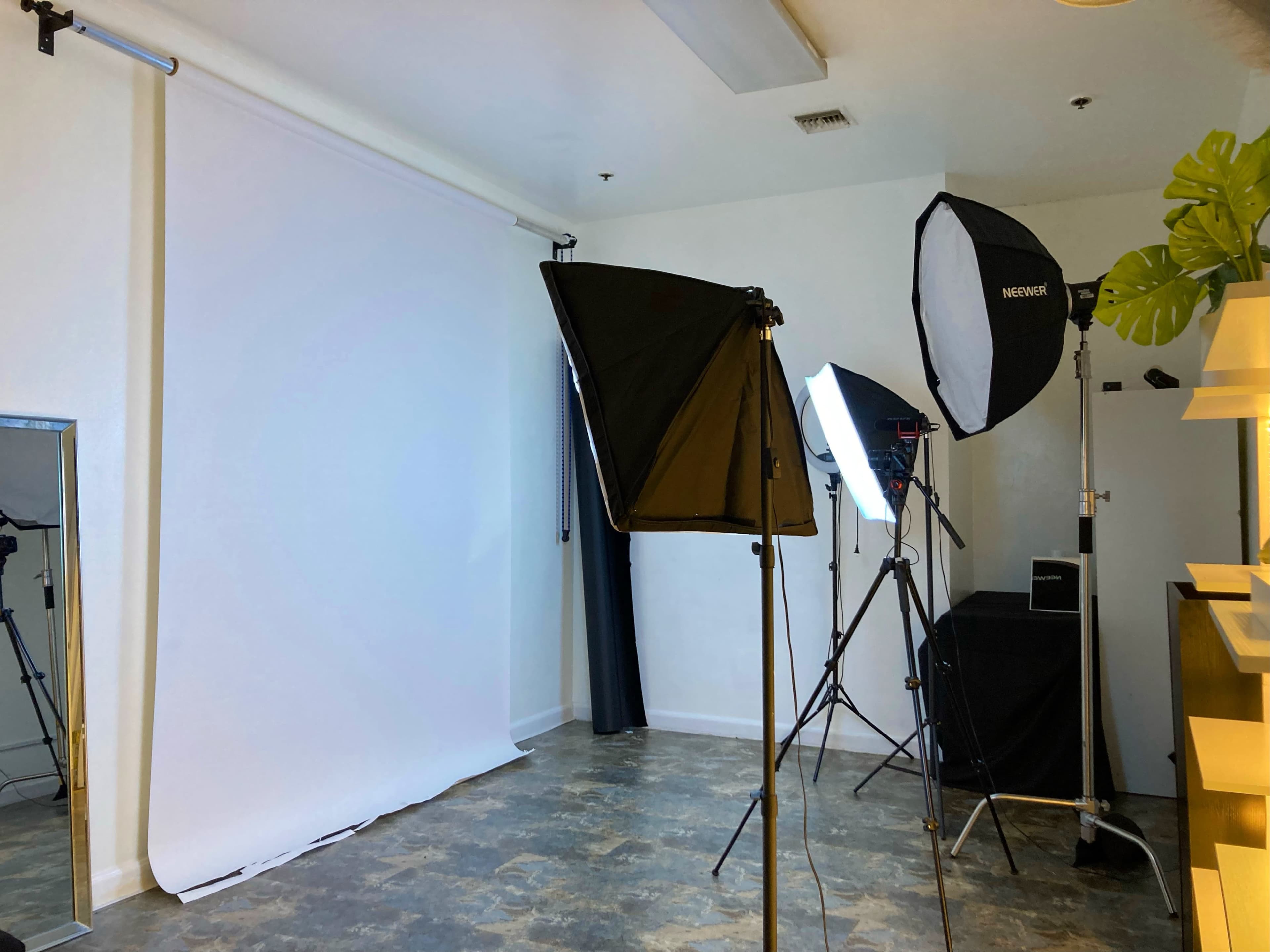 A photography studio setup with softbox lights, a white backdrop, and a mirror in the corner.